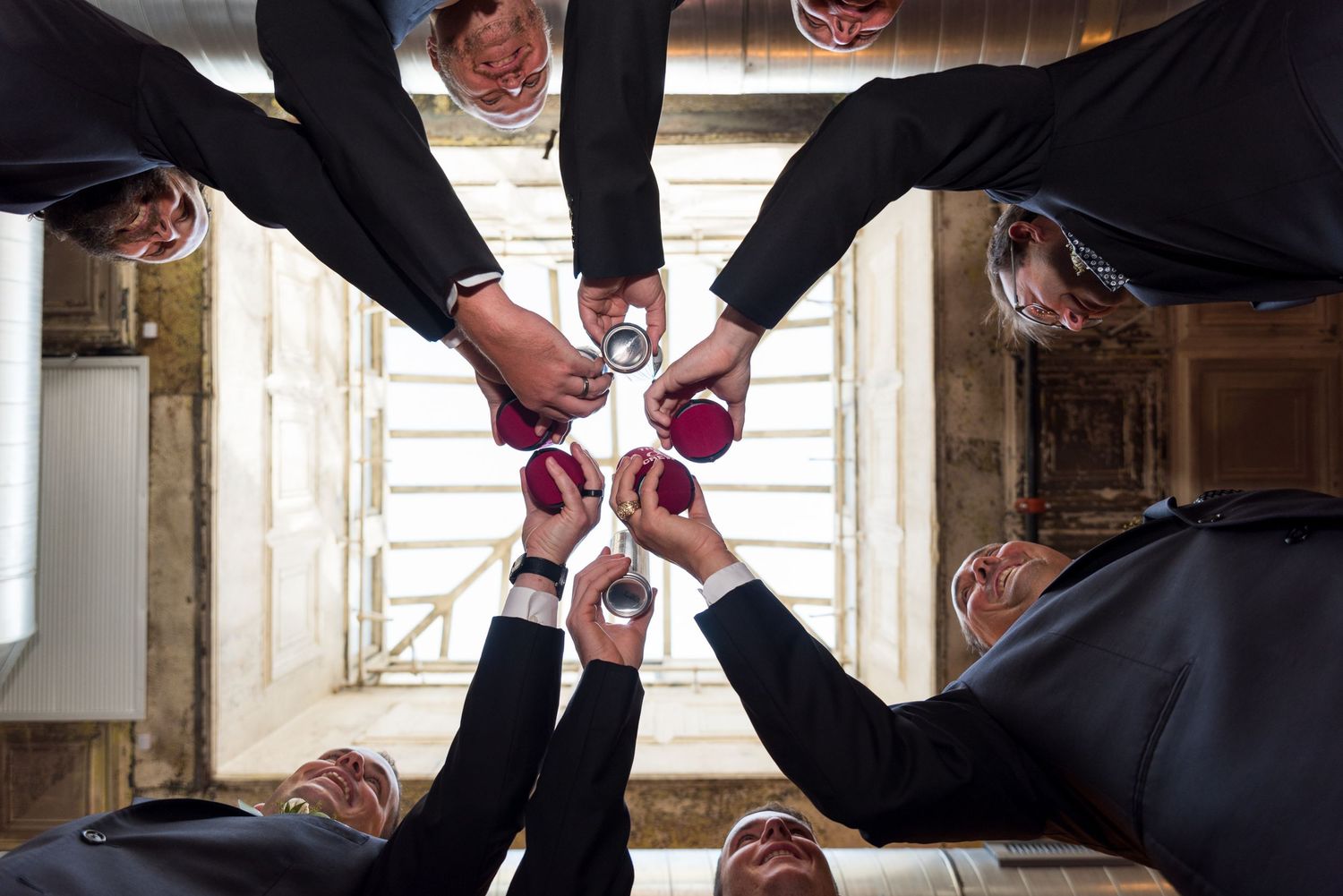 groom and wedding party groomsmen cheers with cups looking up into skylight at Fort Worth wedding venue
