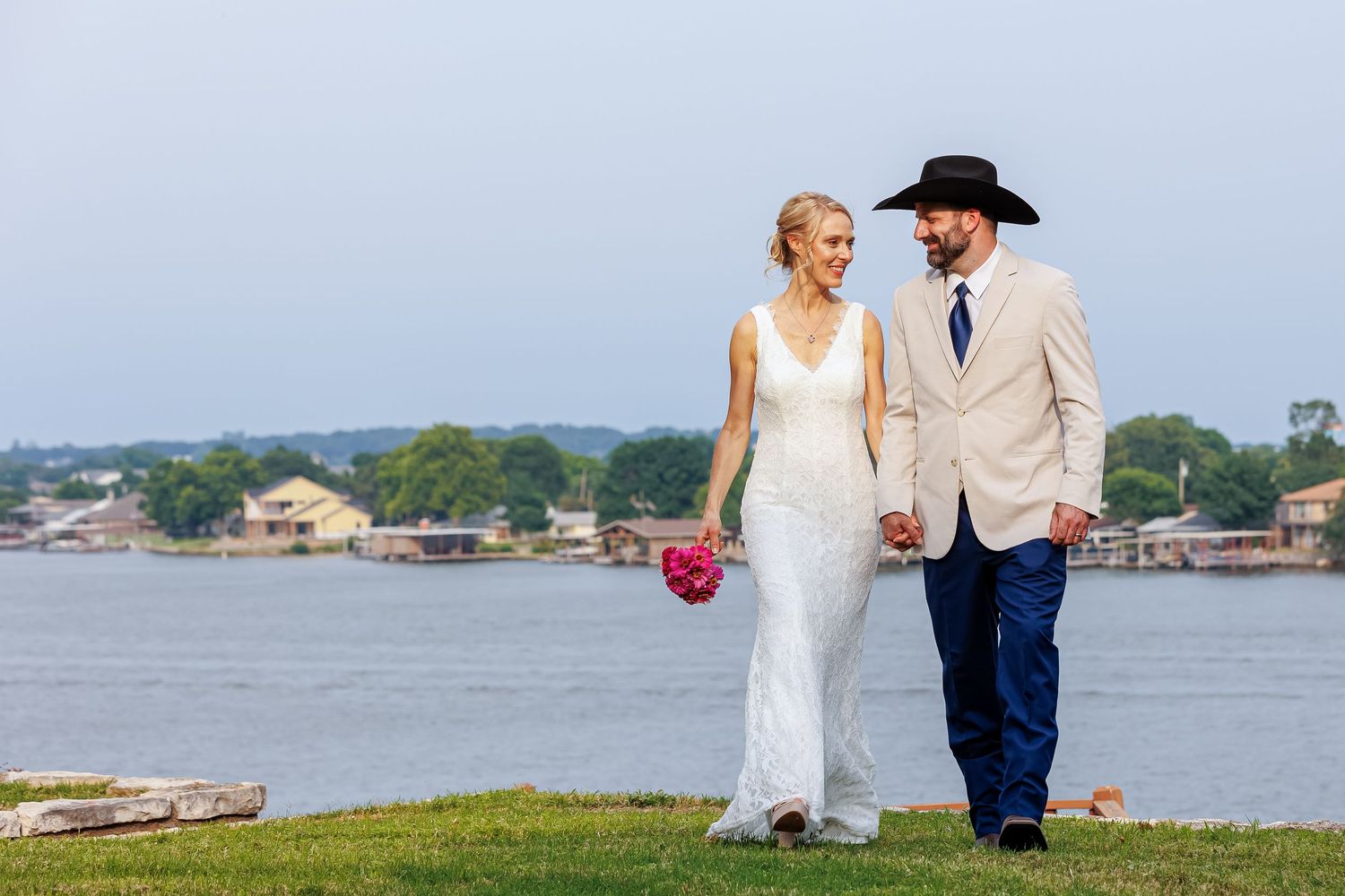 bride and groom holding hands walking on lawn near lake in granbury