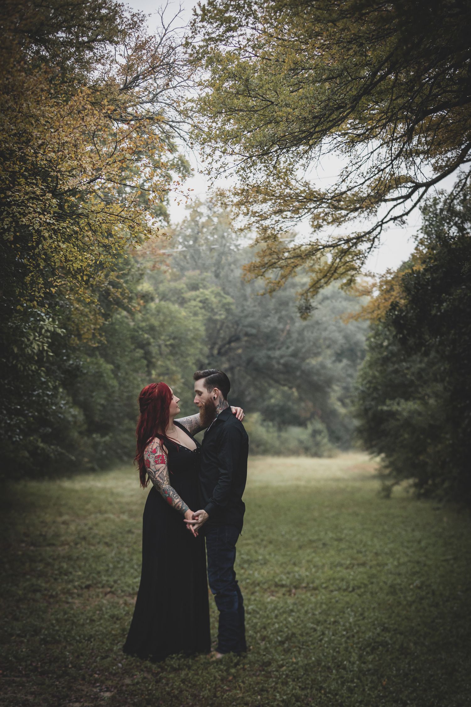 man and women at engagement session surround by dark green foliage and misty rain