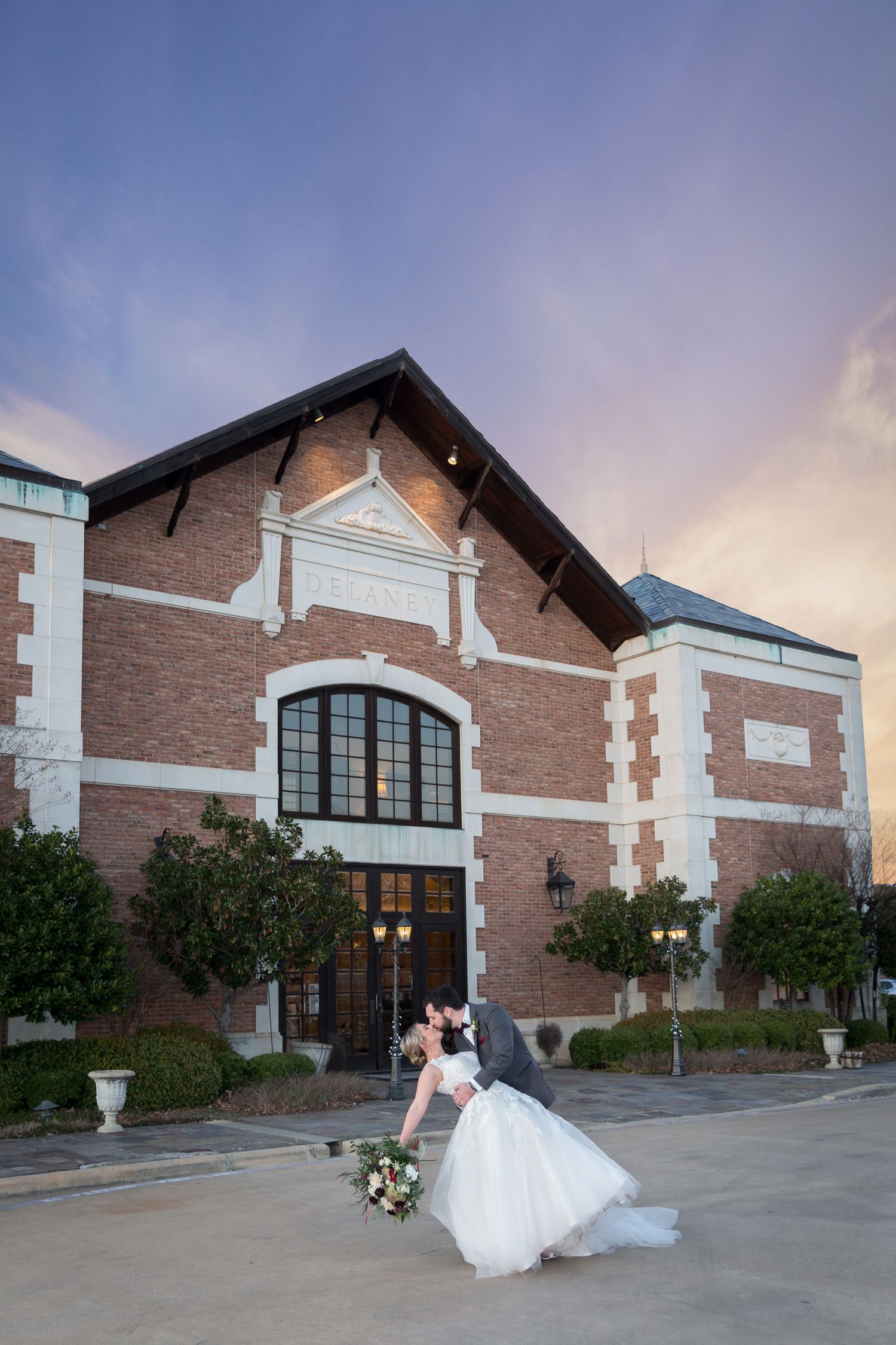 bride and groom dip kiss at sunset in front of winery