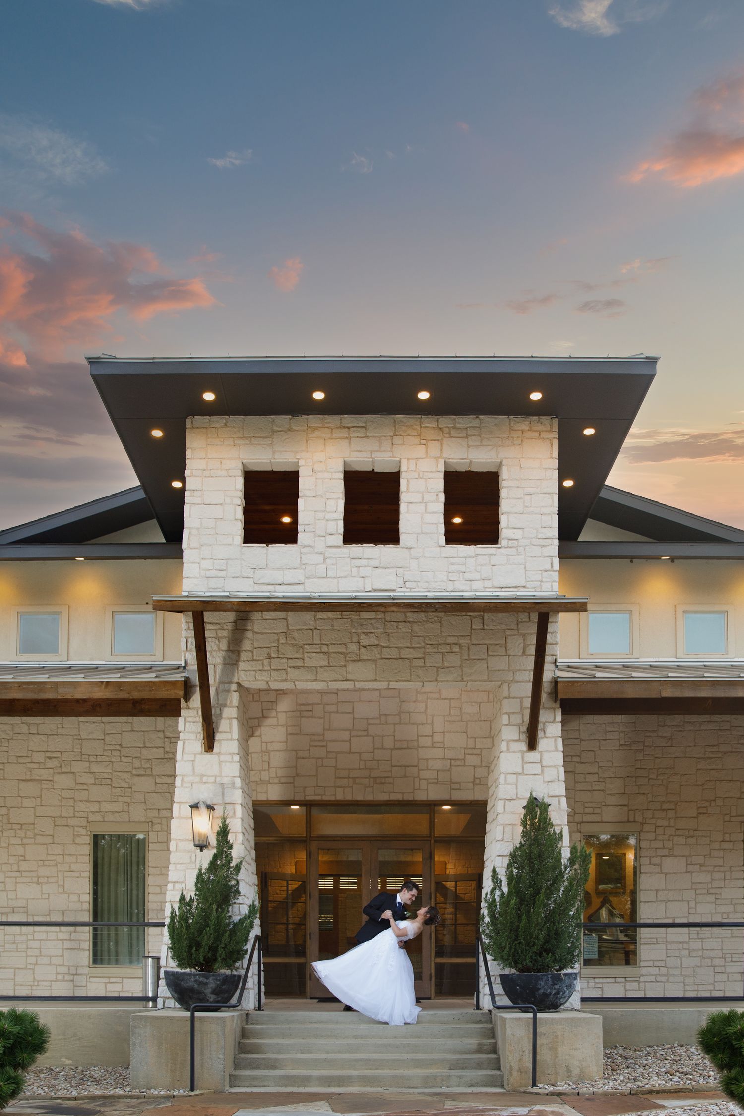 bride and groom at sunsets in front of walters wedding venue dipping kiss