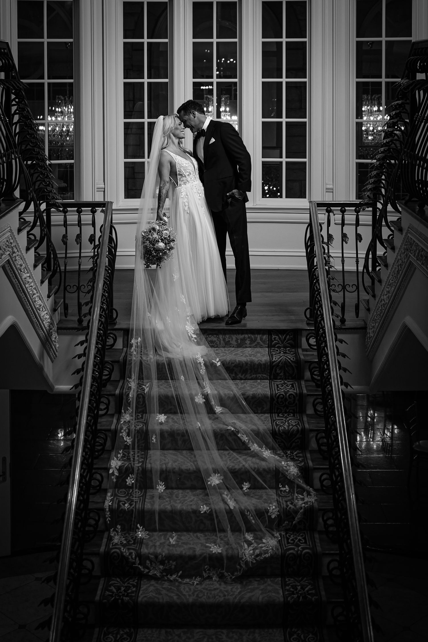 black and white photo of bride and groom on the stairs of The Olana Walters Wedding venue with veils down stairs