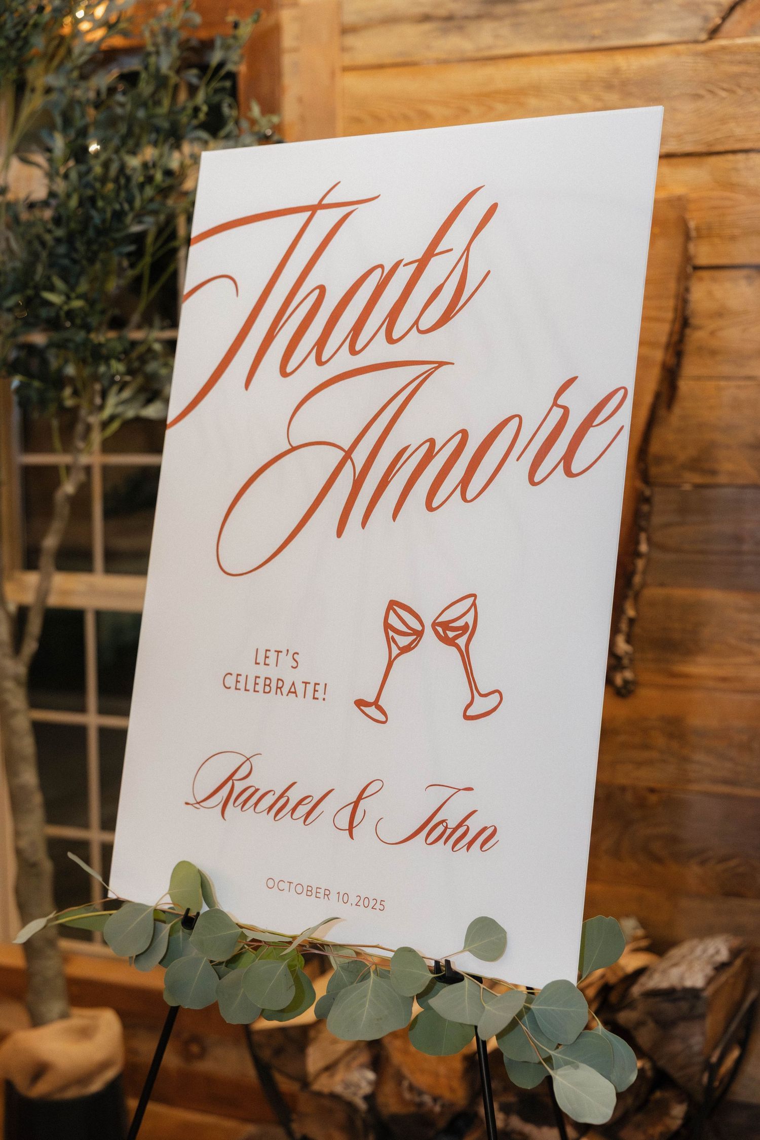 Elegant wedding signage with copper calligraphy and eucalyptus leaves against wooden backdrop.