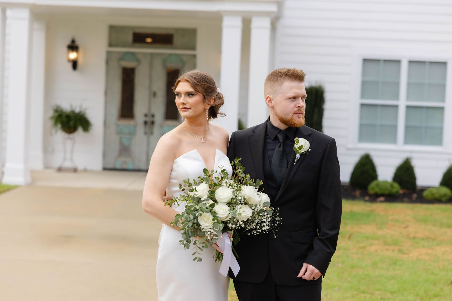 Wedding party walks along white colonial style building exterior.