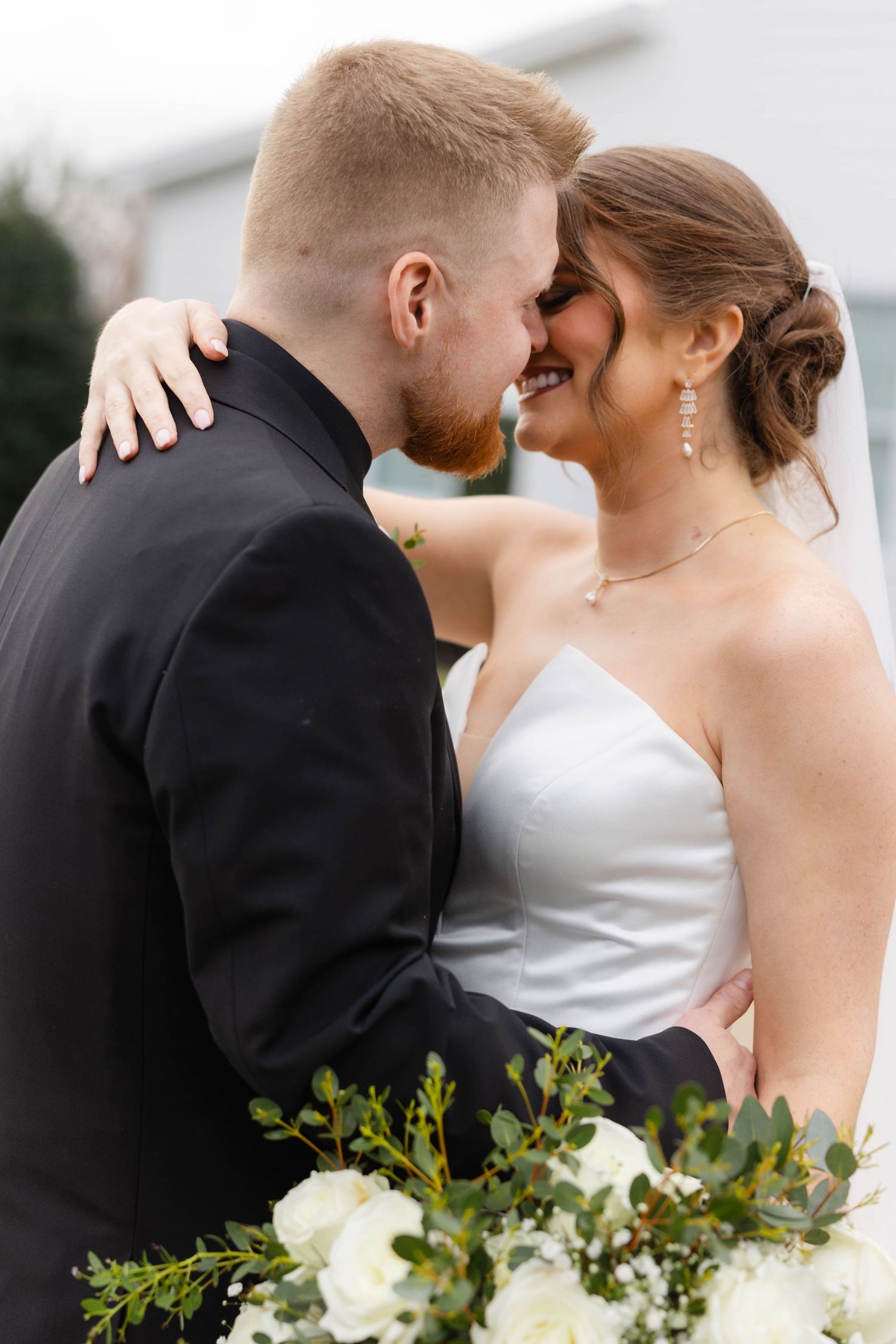 An intimate wedding portrait capturing a tender moment between newlyweds with white floral bouquet details.