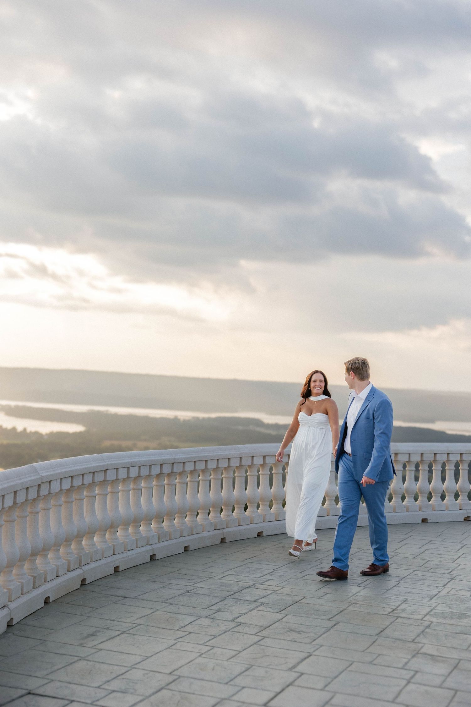 Couple enjoying sunset view from stone terrace overlooking mountain landscape.