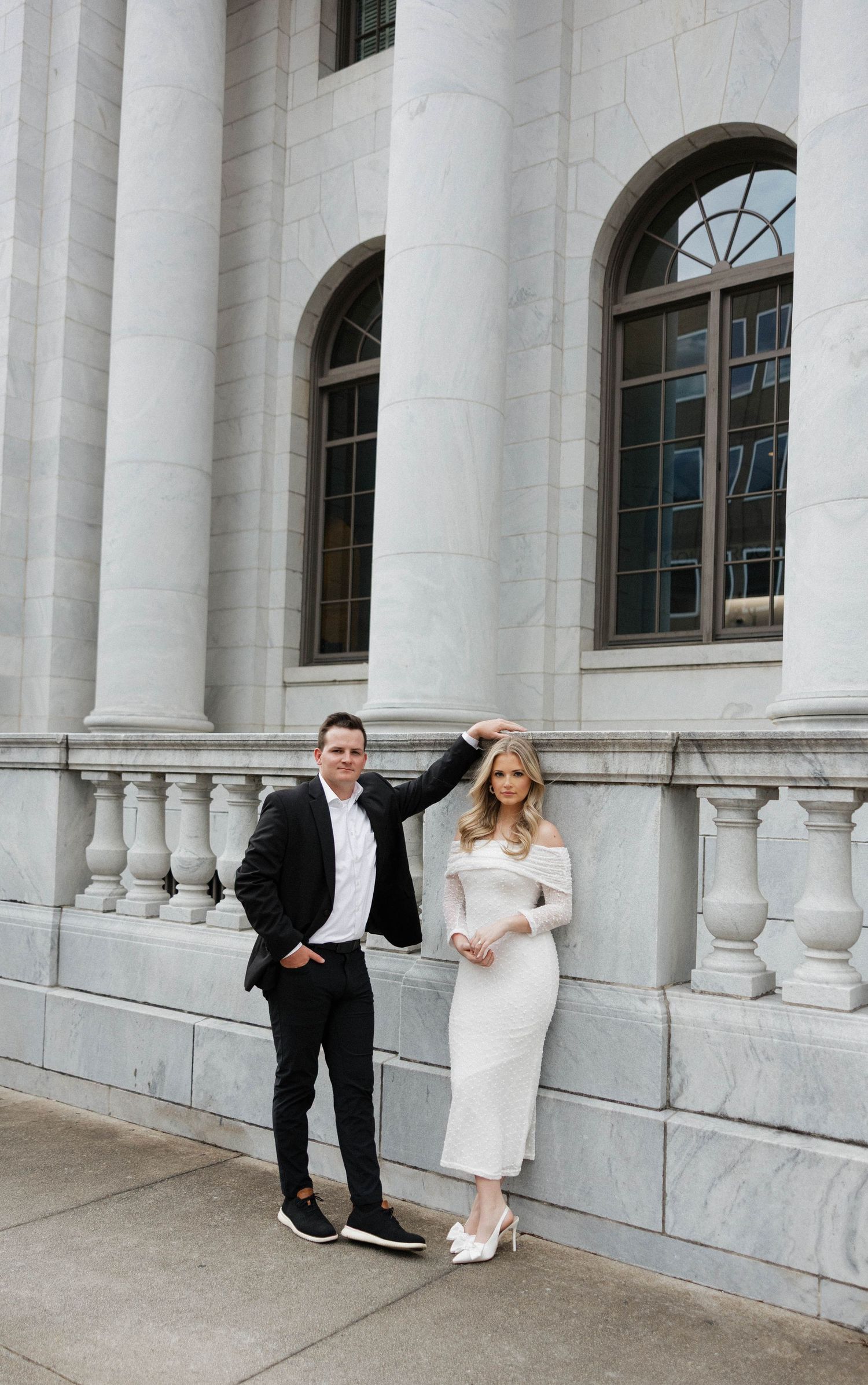 A couple poses playfully on white stone steps of a classical building with columns.
