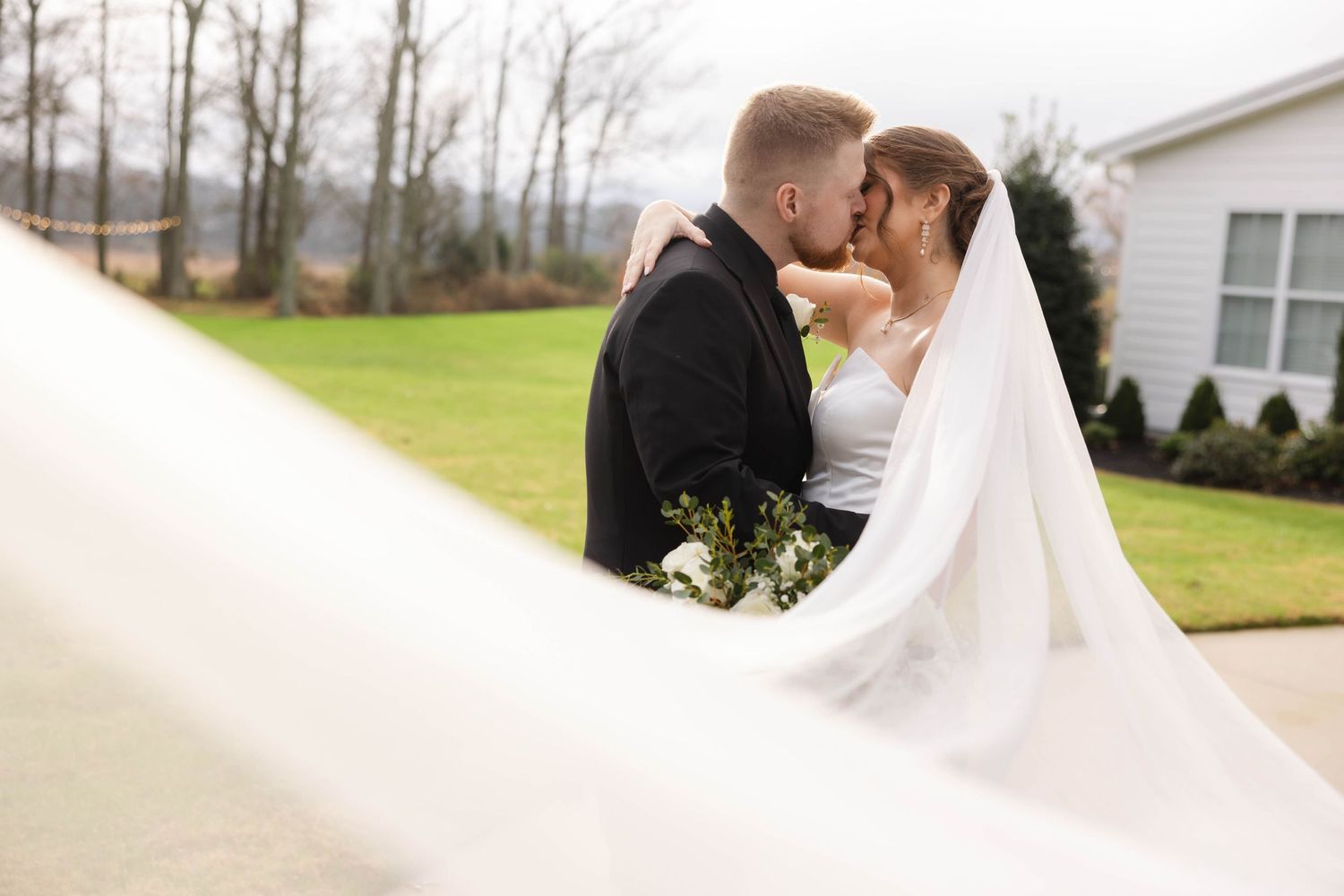 A romantic wedding photo showing a couple embracing outdoors with the bride wearing a flowing white veil.