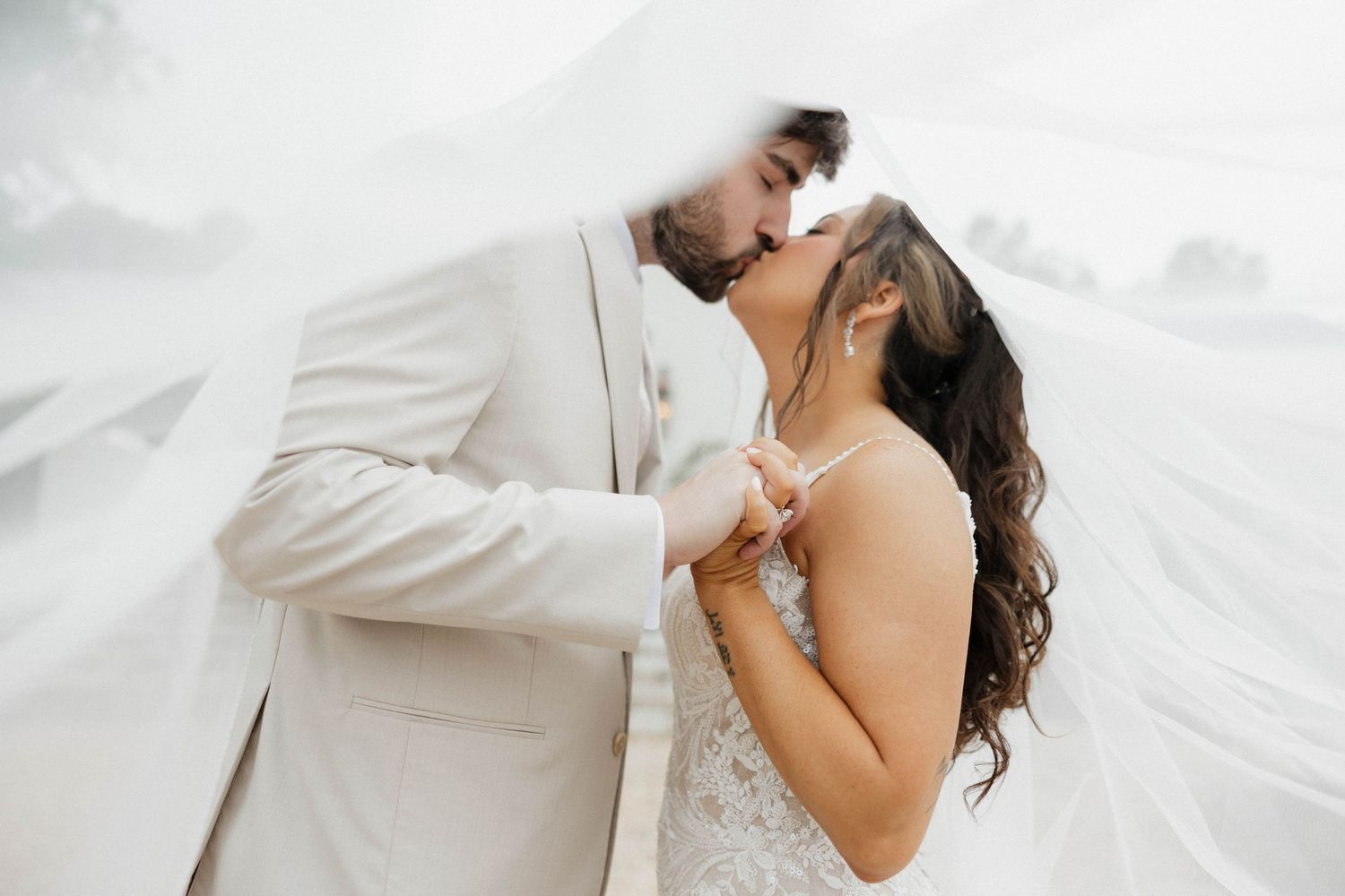 Intimate wedding moment captured with flowing white veil in soft light.