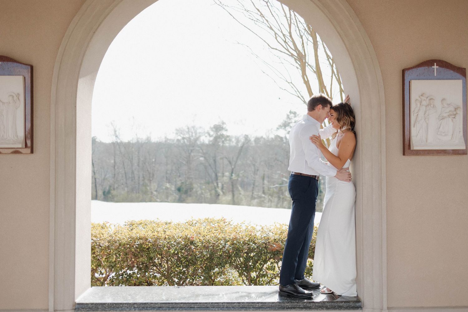 A couple in wedding attire shares a romantic moment under an arched colonnade with scenic views.