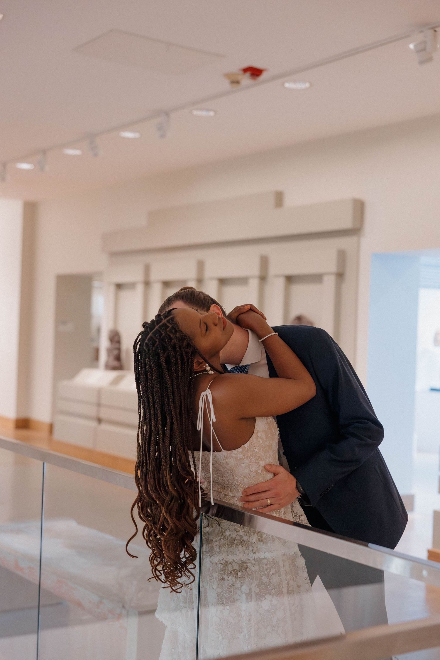 A romantic embrace between a couple in wedding attire at an art gallery.