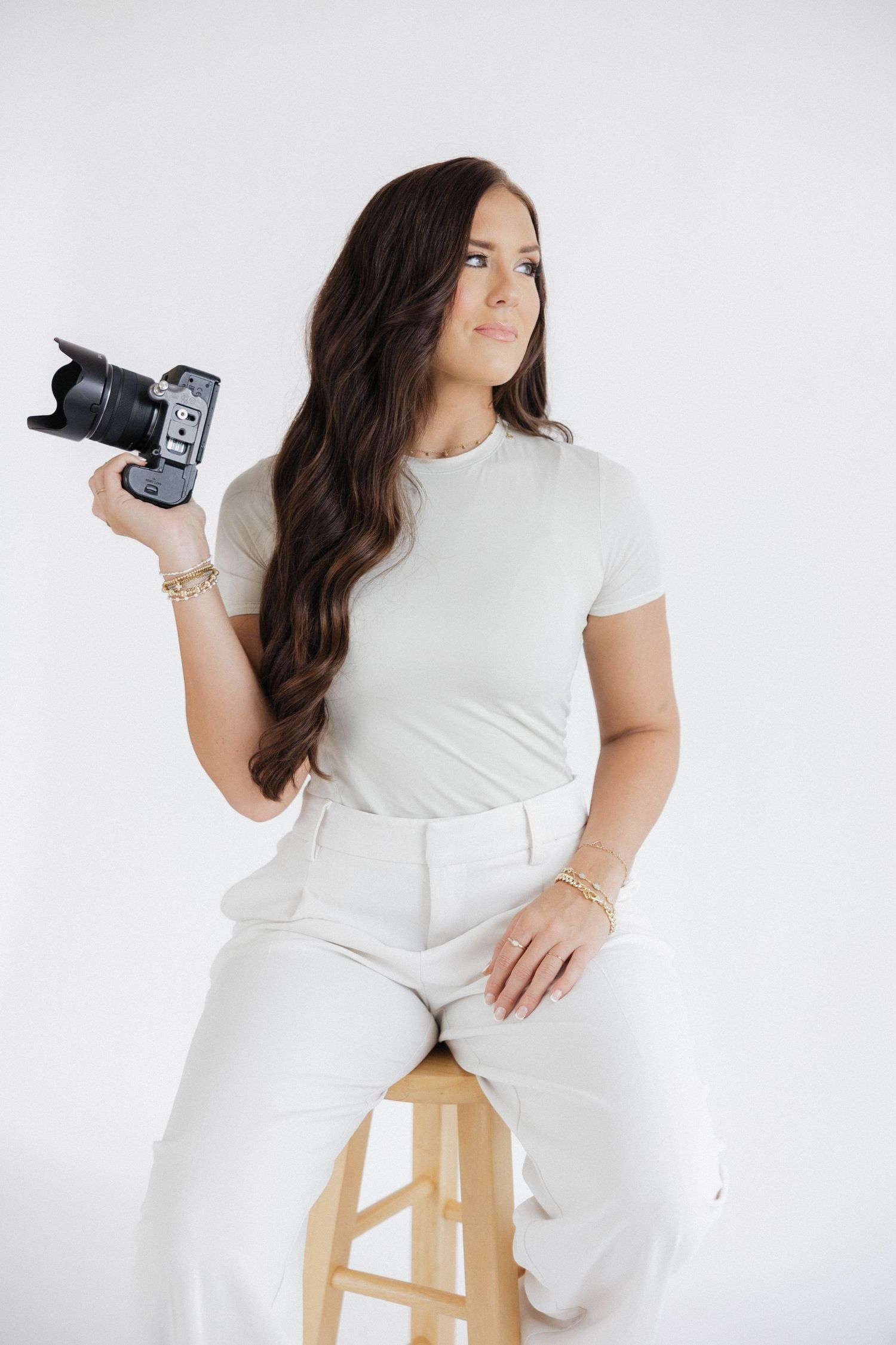Professional photographer in white outfit poses with camera against light background in creative studio setup series.