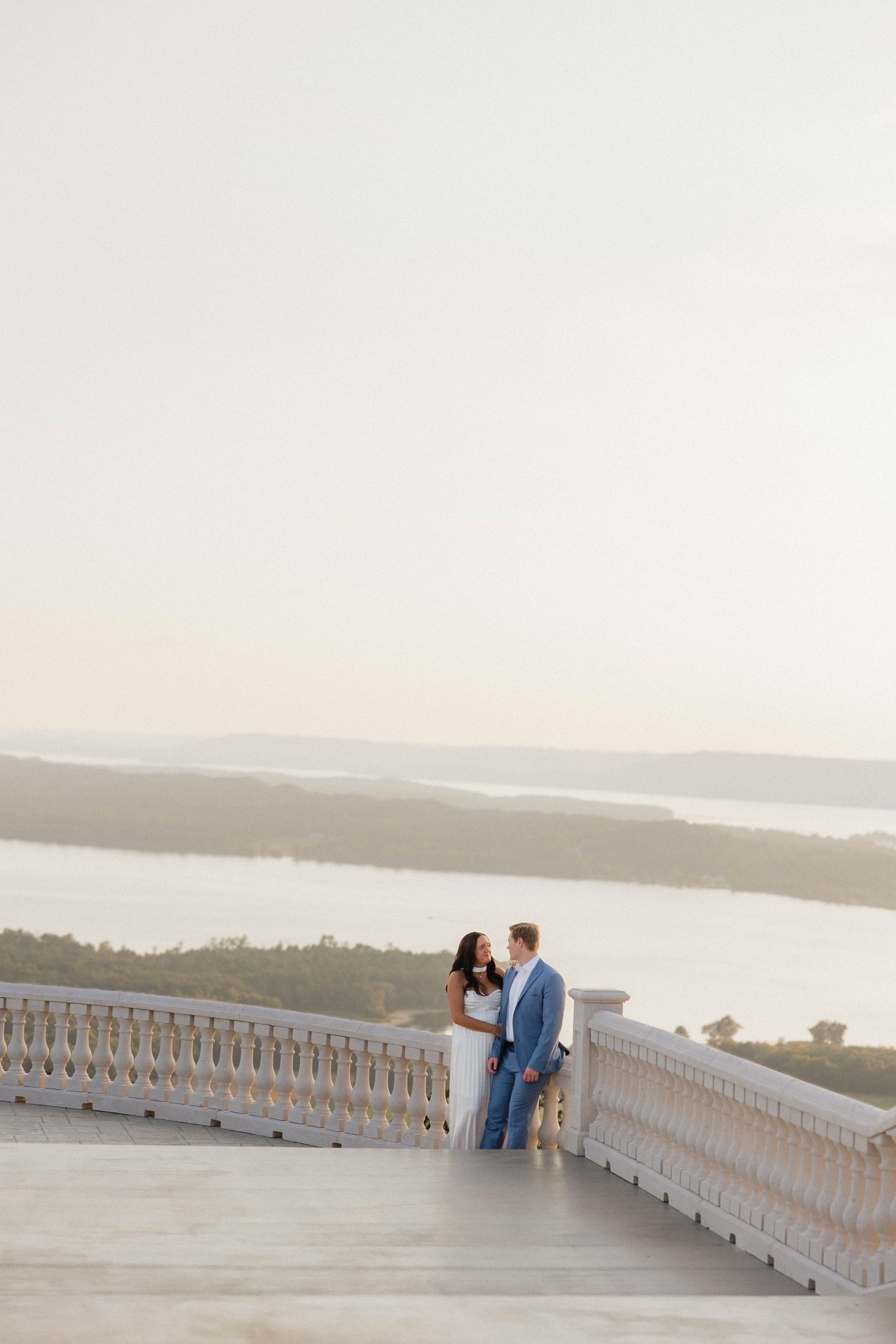 Couple sharing intimate moment on white stone balcony overlooking scenic vista.