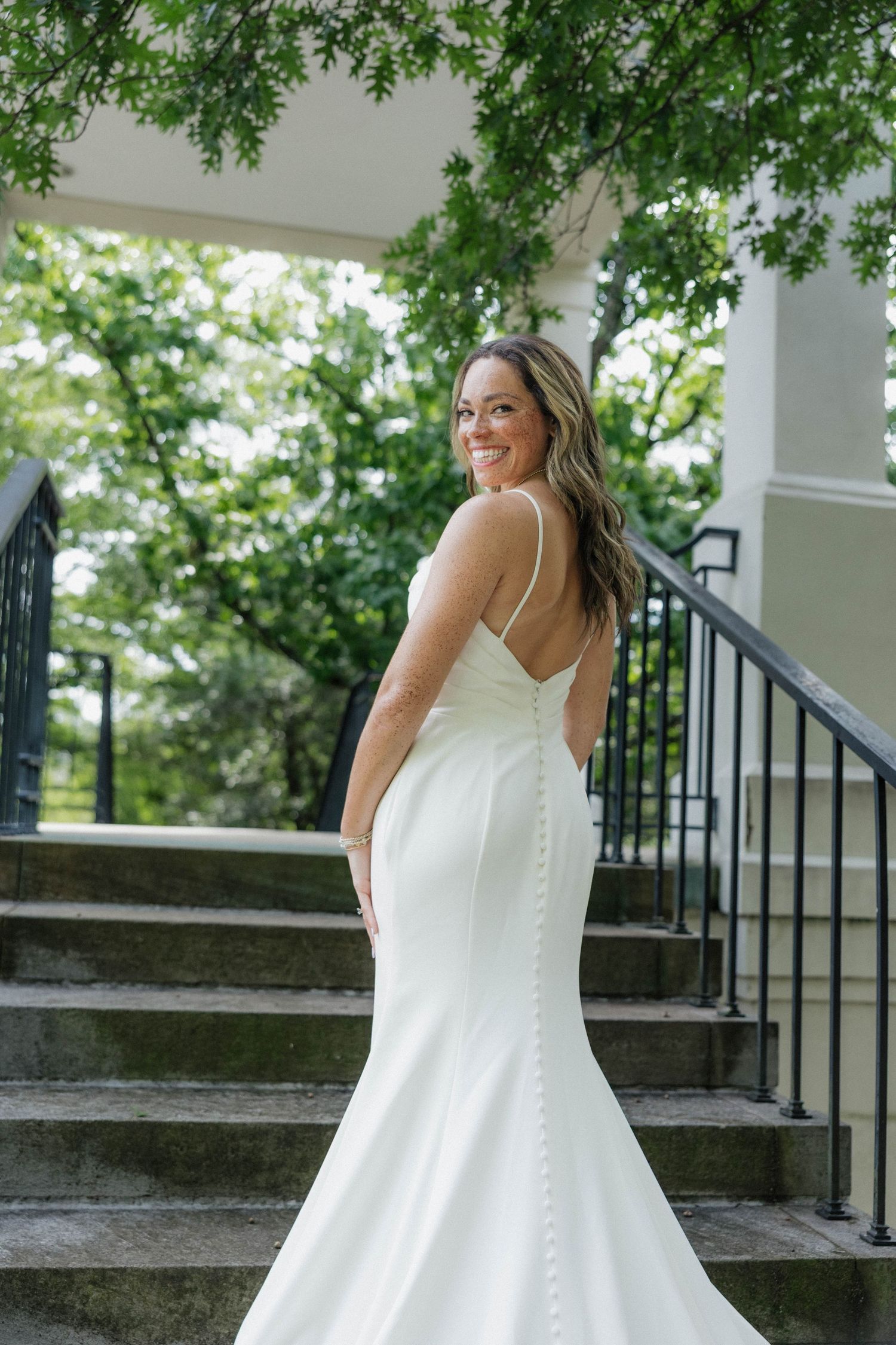 Classic white wedding gown with buttons photographed on outdoor stone steps.