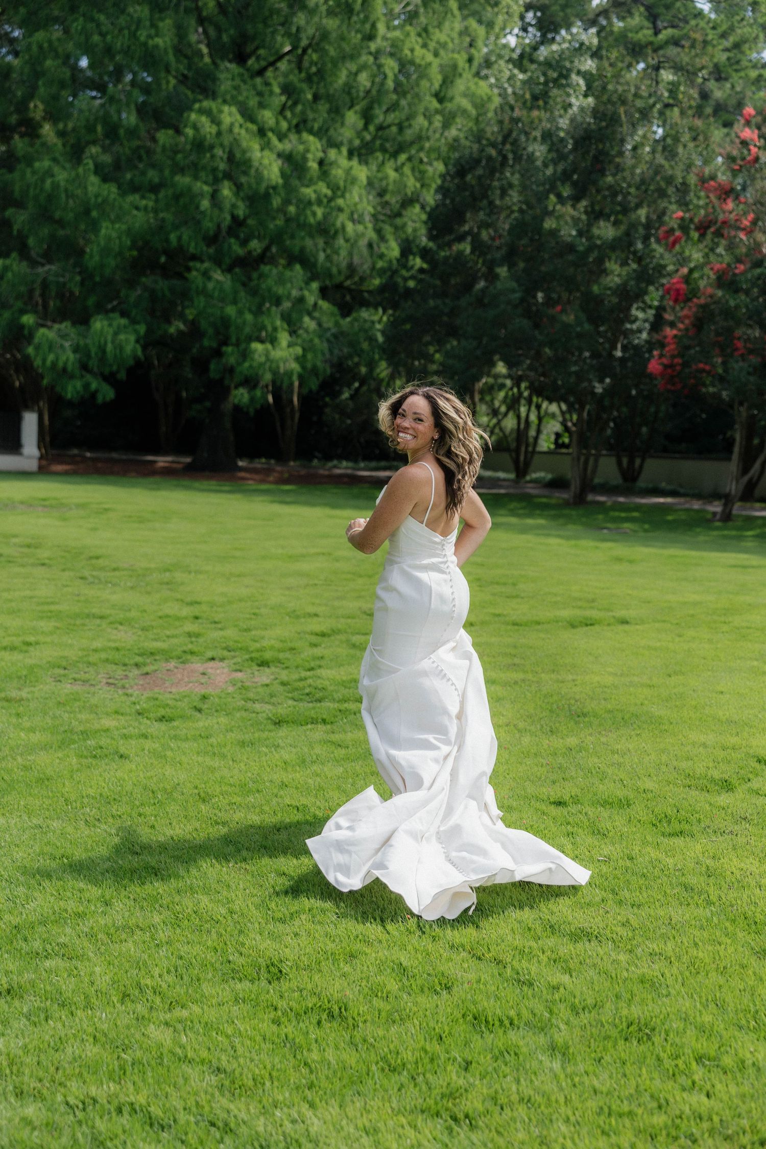 Sequence of person in white dress twirling on green lawn with trees in background.