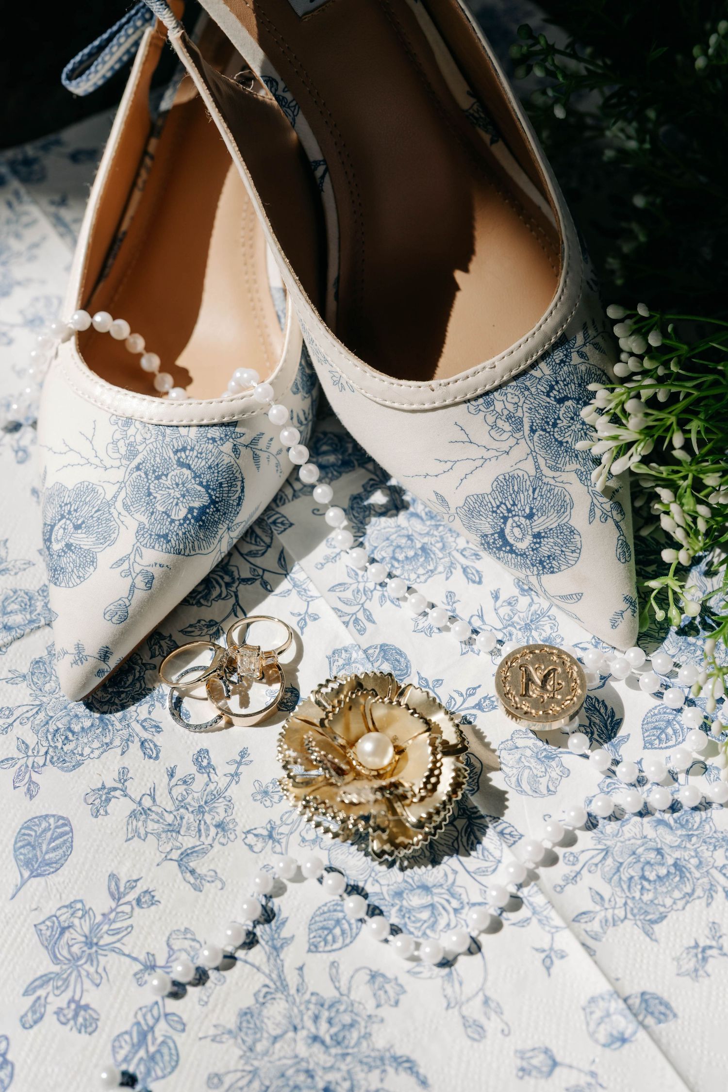 Wedding accessories featuring blue and white floral shoes with gold jewelry and rings.