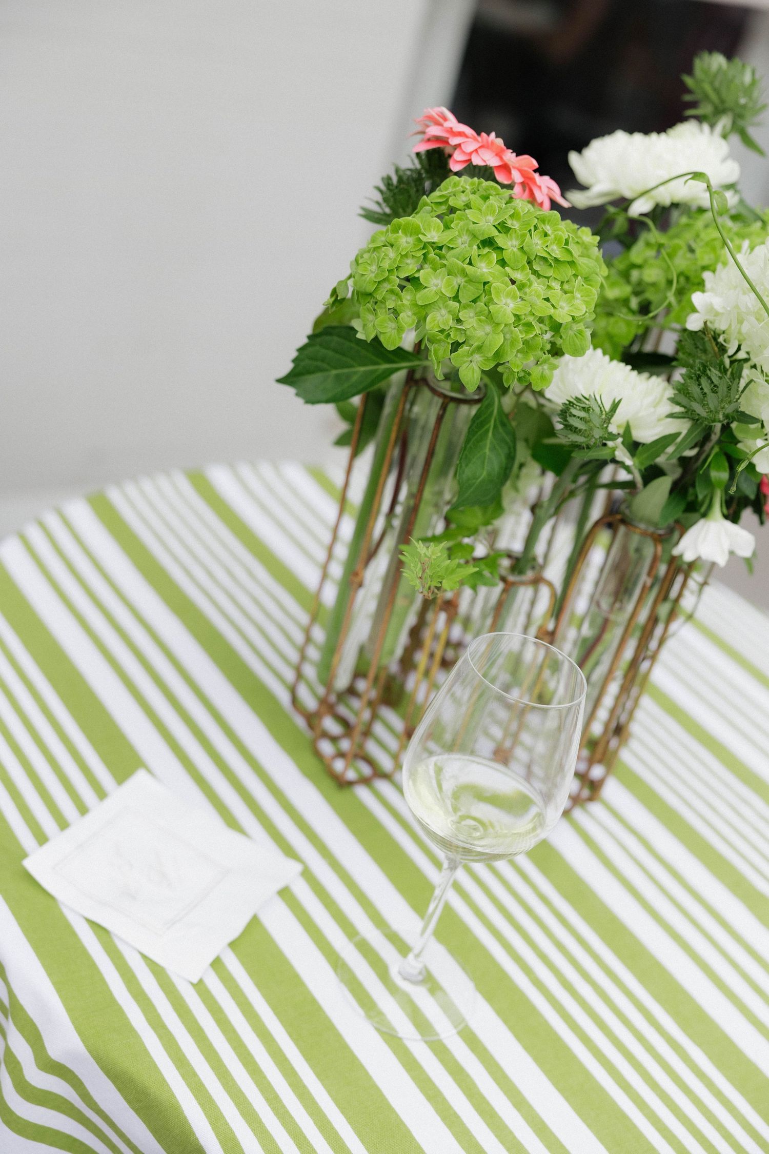 Green and white floral arrangements on striped tablecloths create an elegant table setting.