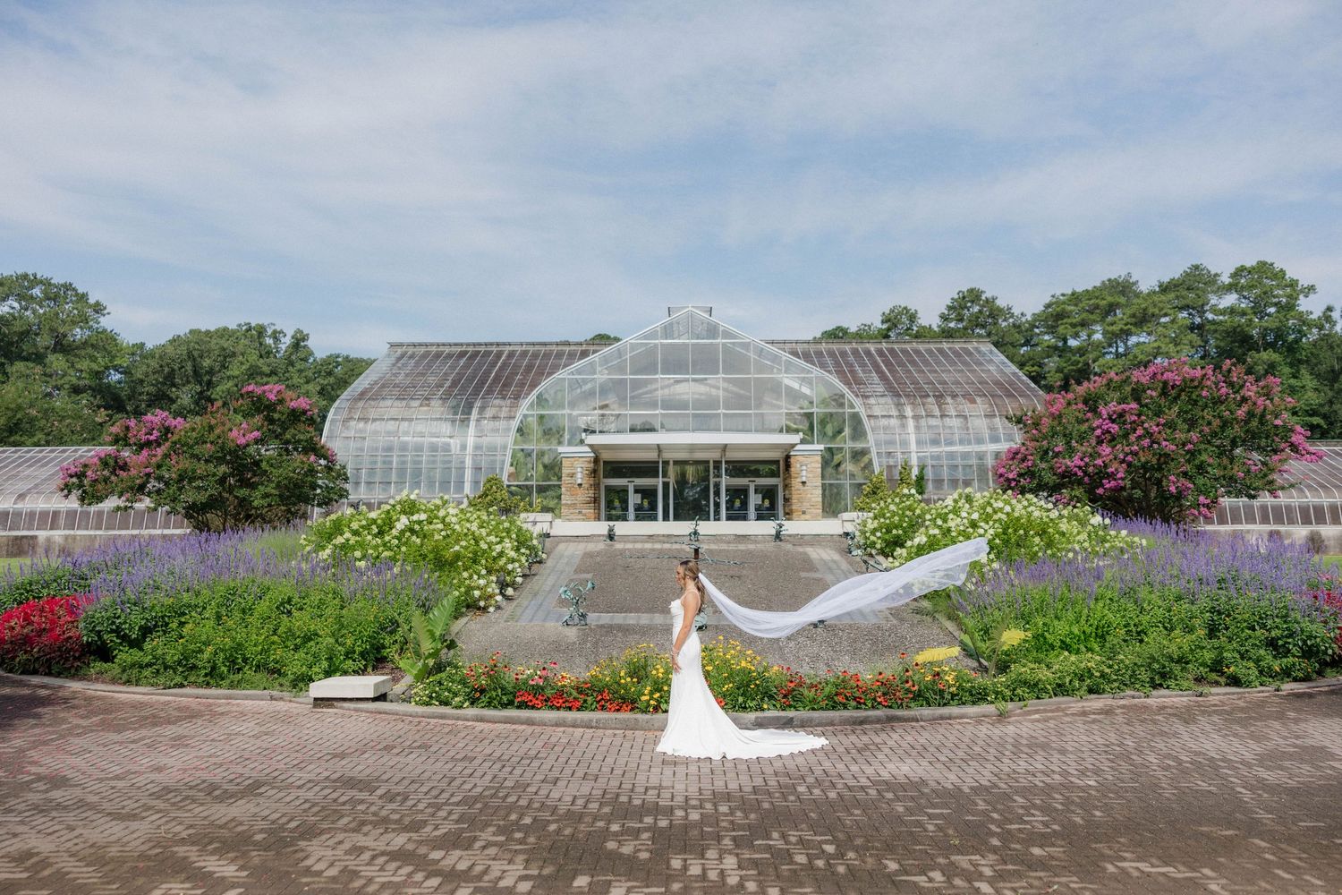 Panoramic view of greenhouse and gardens with cloudy sky overhead.
