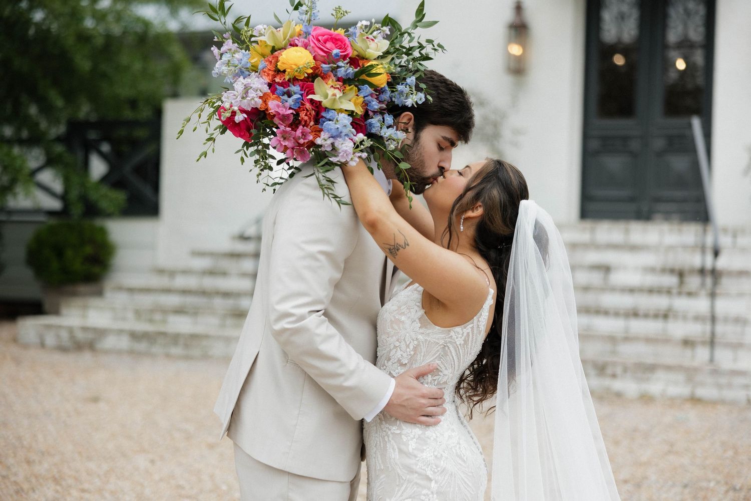 Romantic wedding couple embraces outdoors with flowing veil and floral bouquet.