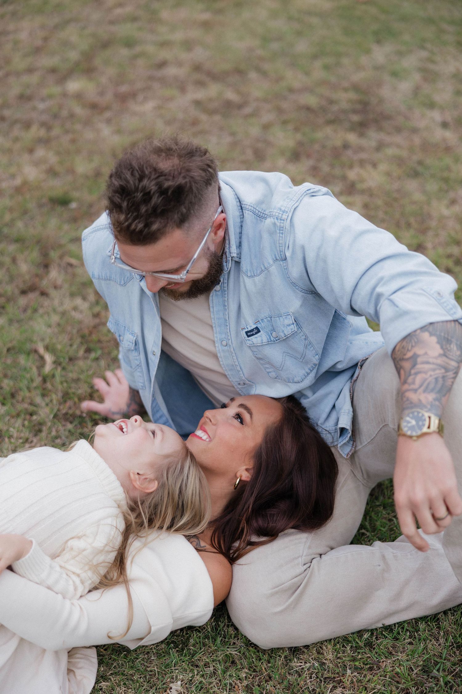 Couple lying on grass taking romantic photos in casual outfits.