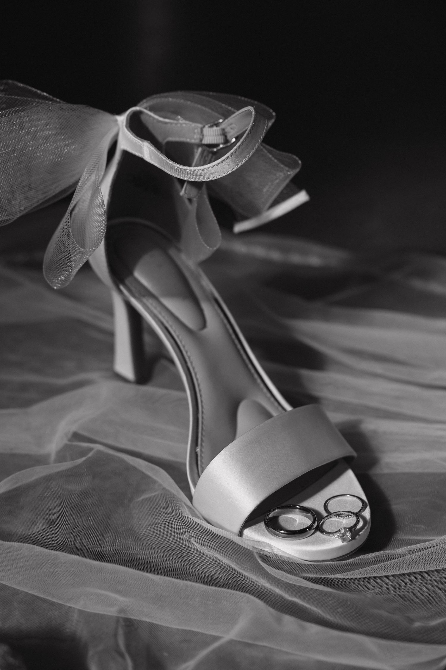 Elegant white bridal shoes with delicate details photographed in dramatic black and white lighting.
