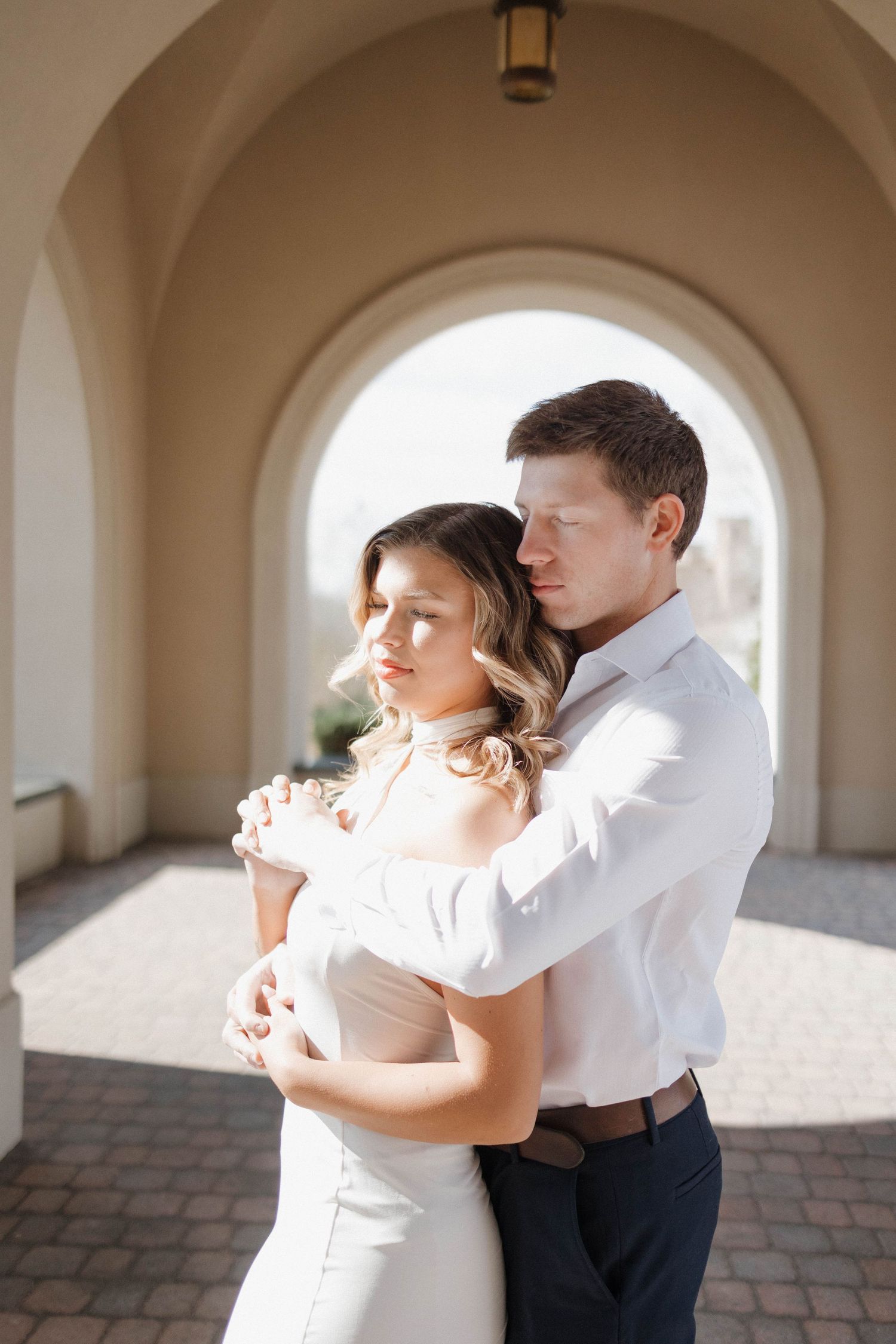 Tender embrace under arched walkway in soft natural light.