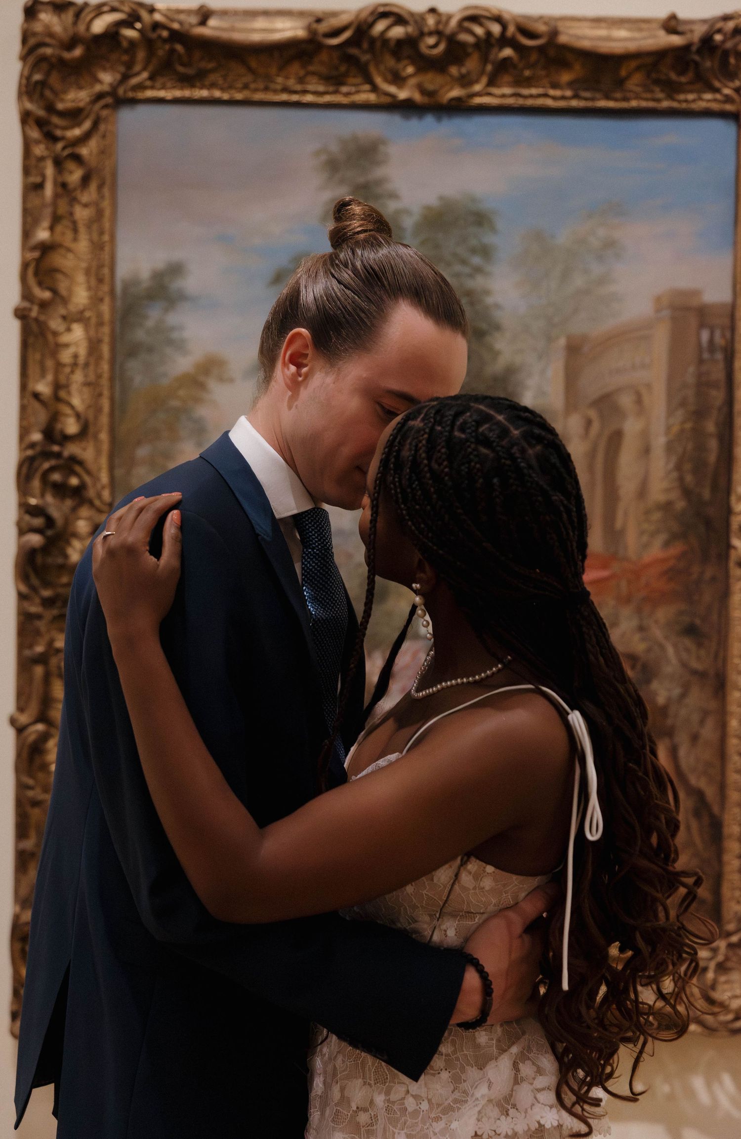 Romantic moment shared between couple in front of ornately framed classical painting.