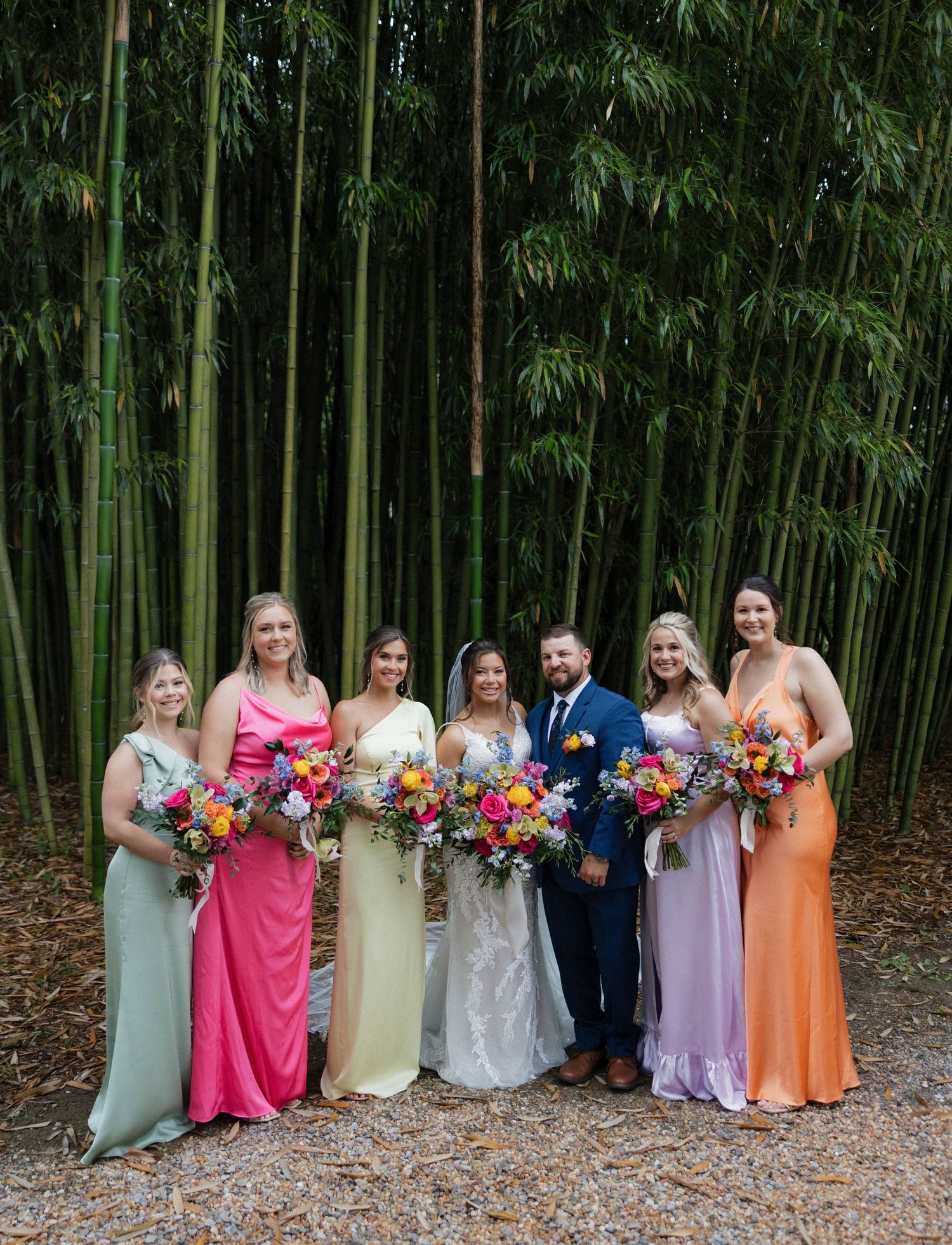 Wedding party in pastel dresses poses in front of bamboo forest.