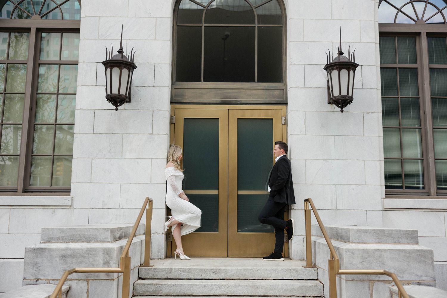 Wedding couple poses in front of an elegant building with lanterns and arched windows.