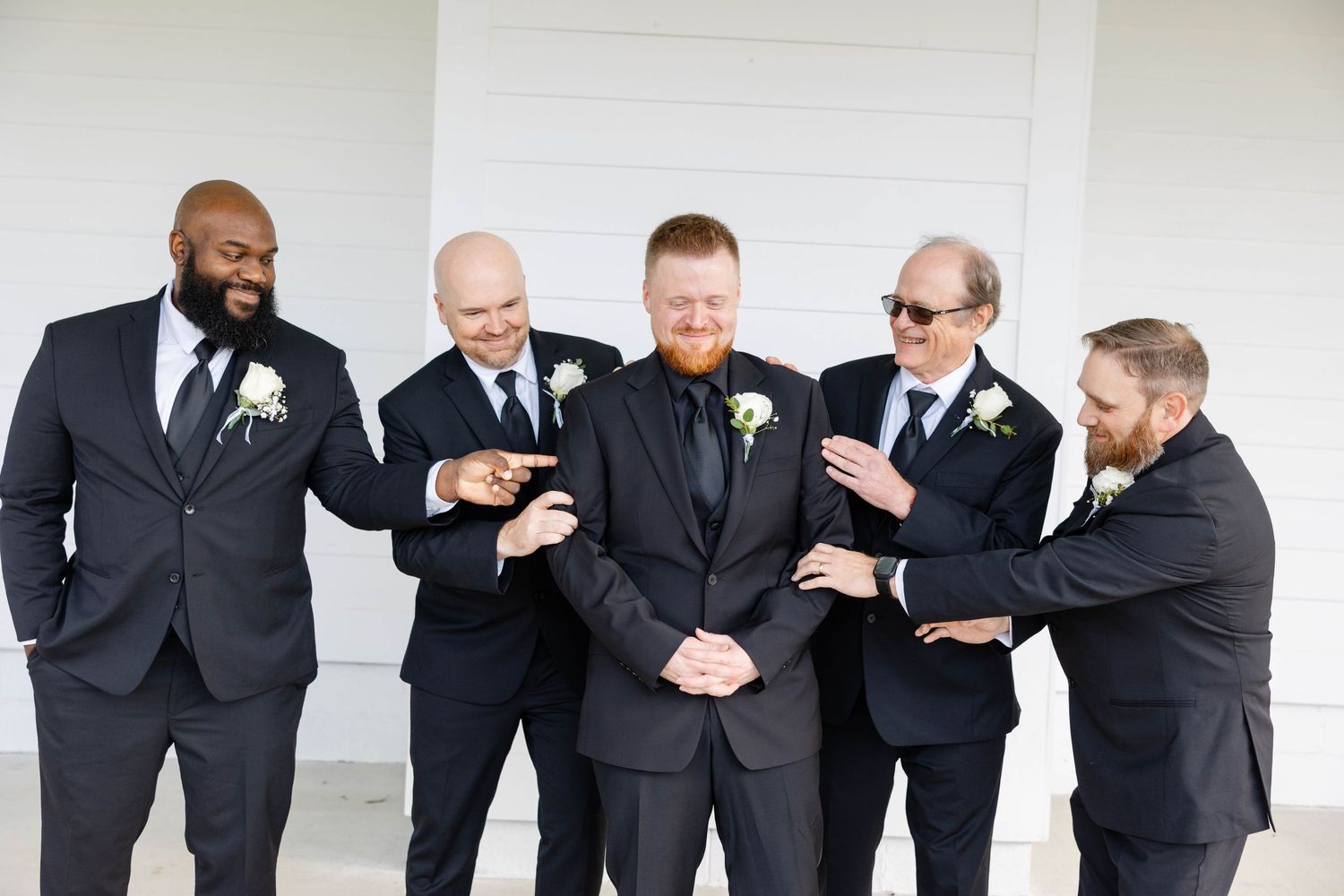 Groomsmen in black suits posing together in casual candid style.