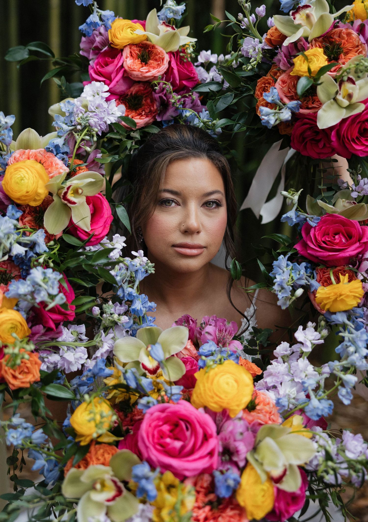 Vibrant floral arrangement with pink roses, yellow ranunculus, and blue delphinium creates colorful frame.