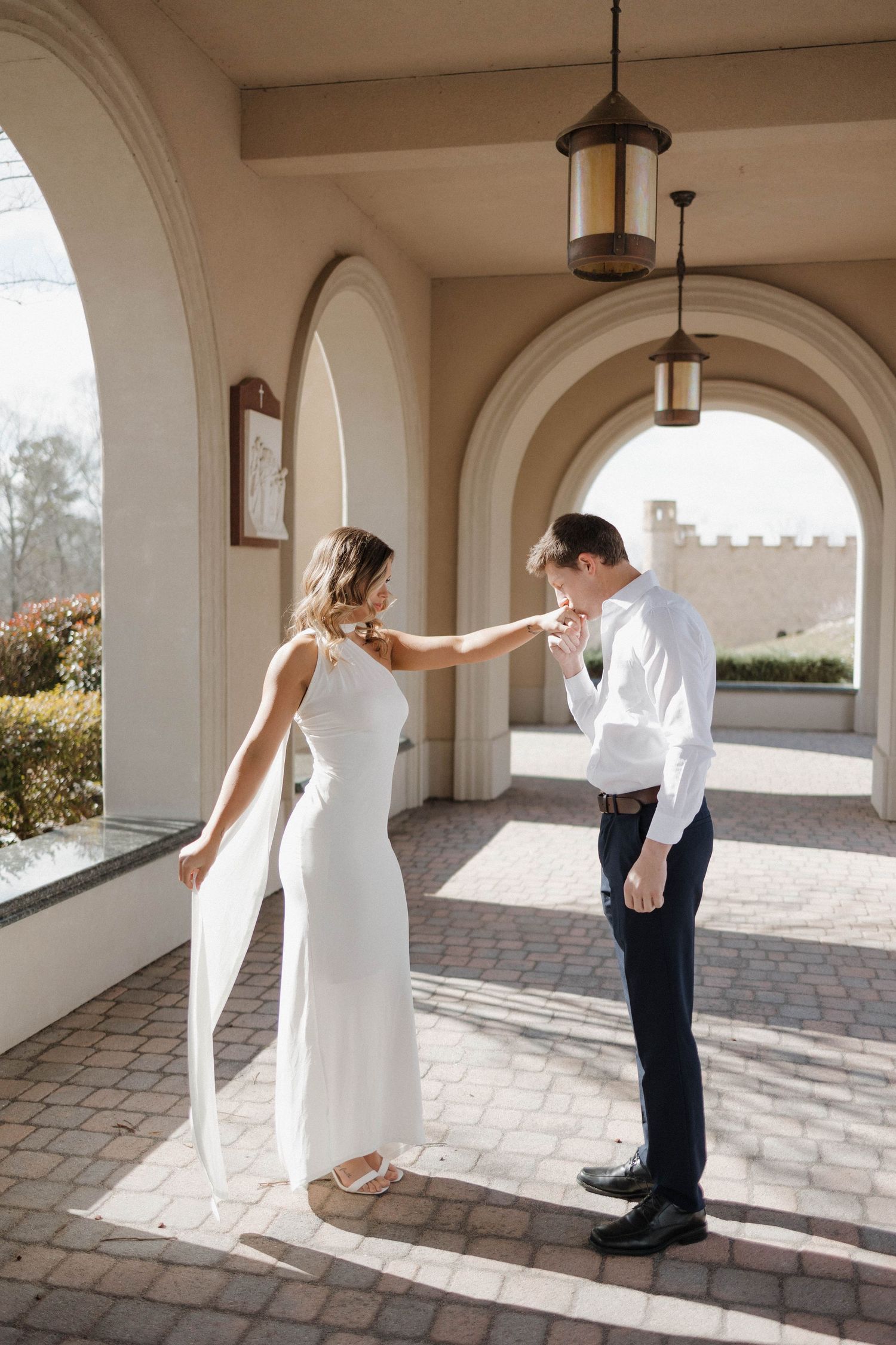 Playful moment between couple in elegant arched hallway with castle view.