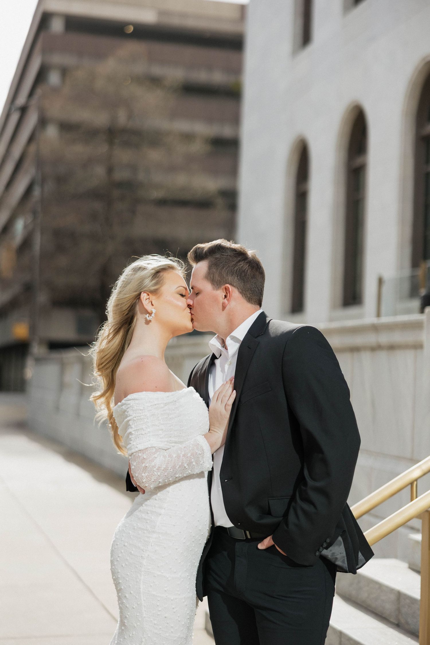 Wedding couple shares romantic kisses against classic architectural backdrop.
