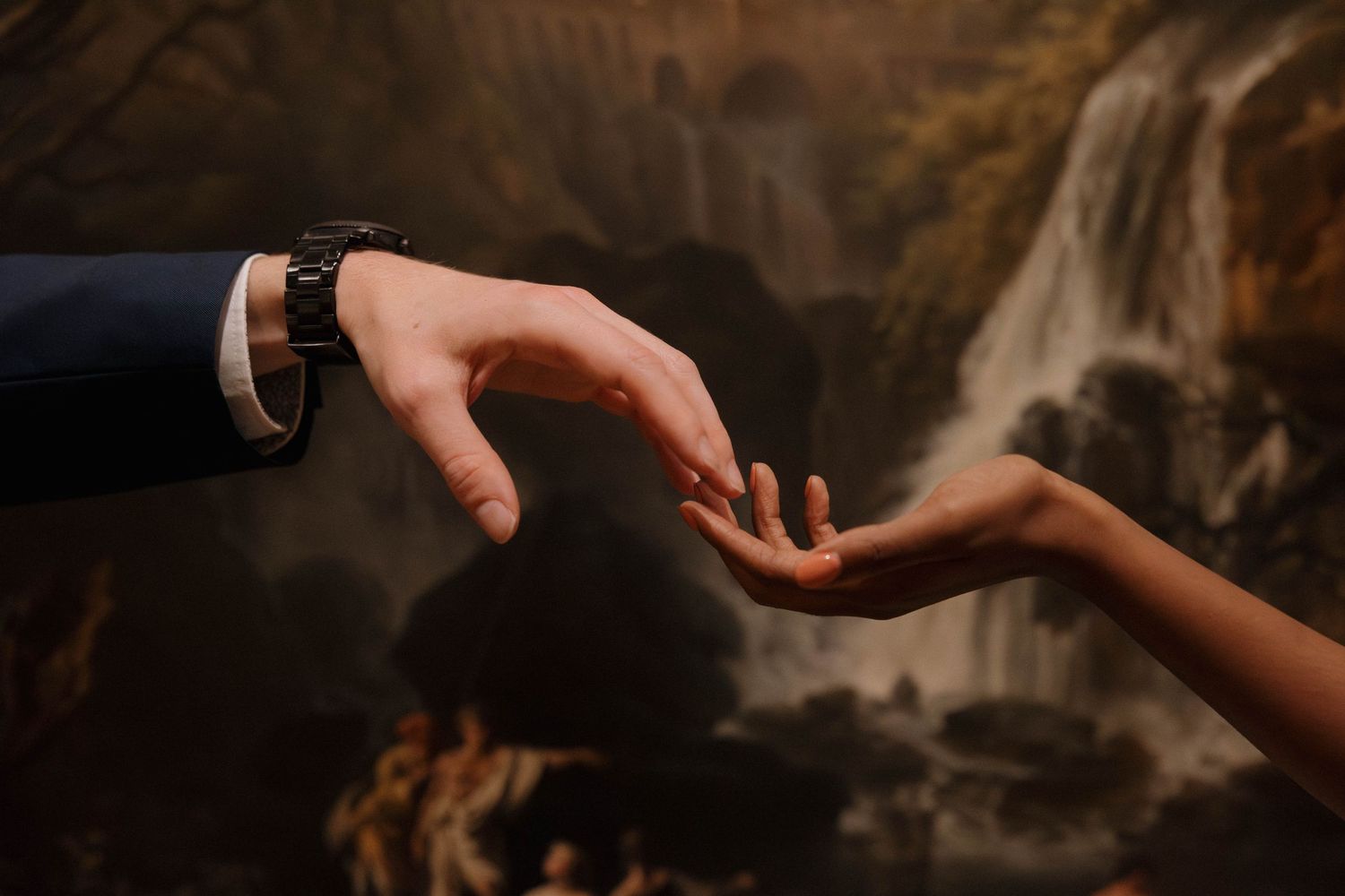 Two hands reaching toward each other against a painted landscape background in dramatic lighting.