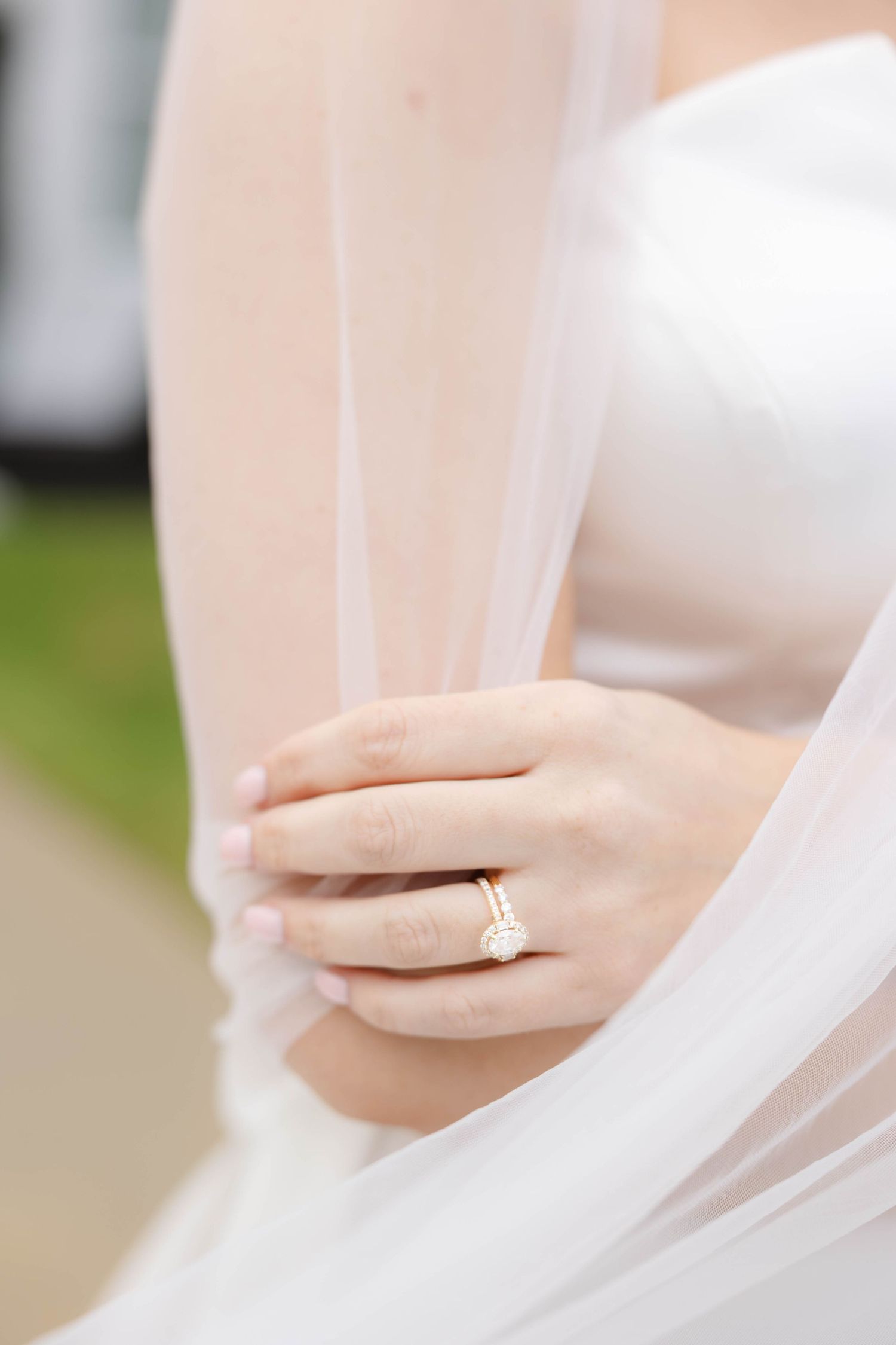 Close-up of bride's hand with engagement ring through delicate white veil.