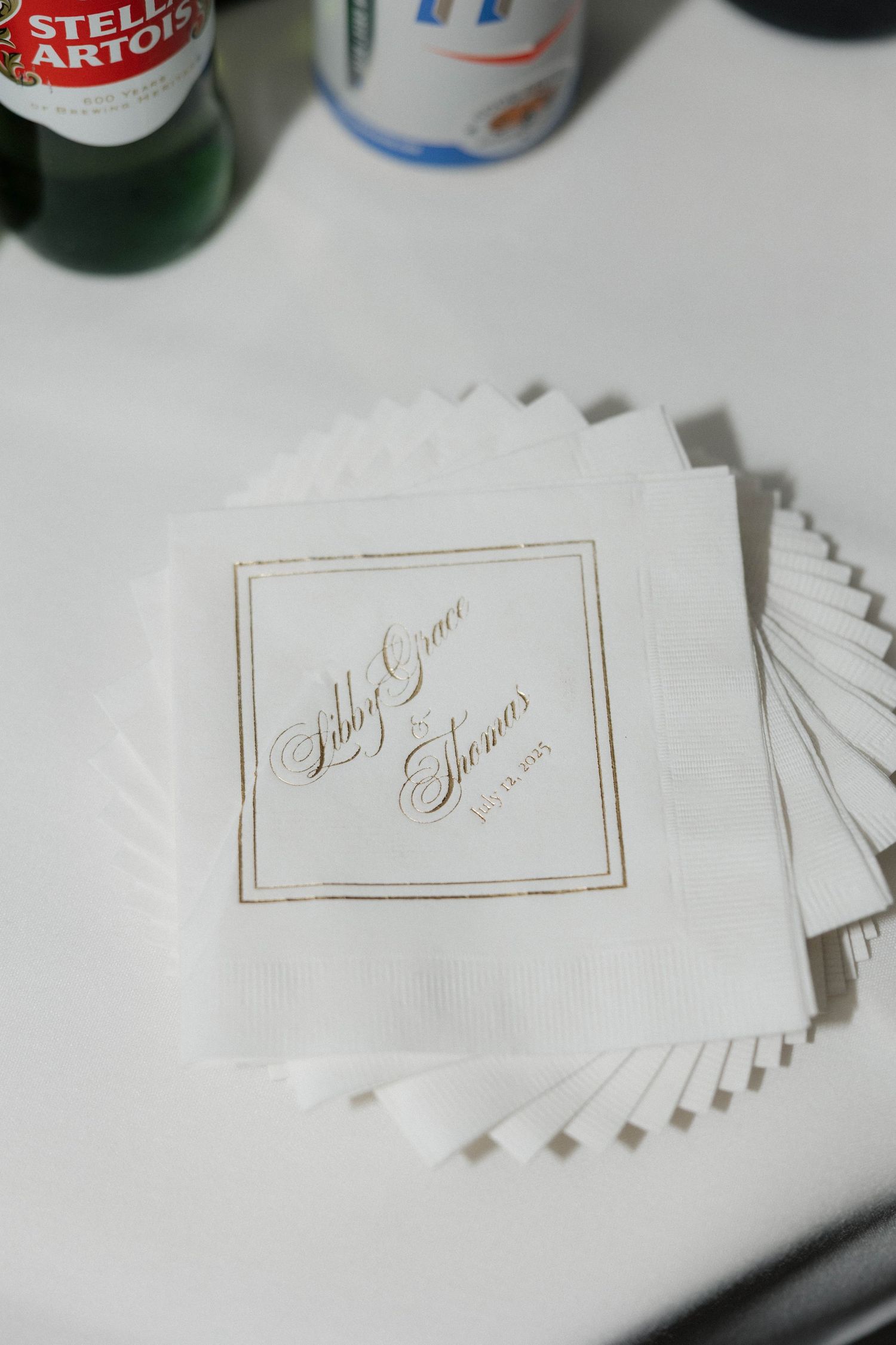 Wedding place cards with gold lettering displayed next to beer bottles.