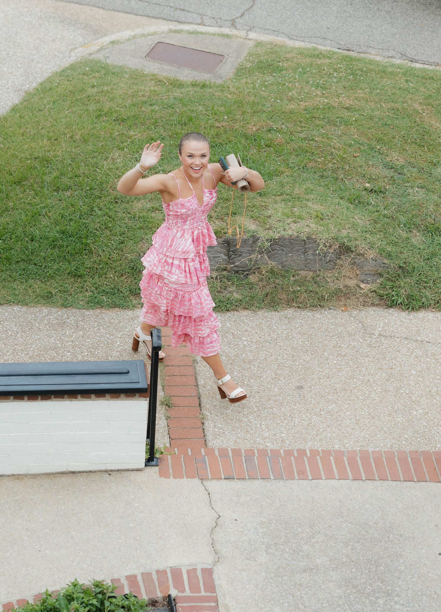 Child in pink ruffled dress plays on outdoor steps in summer.