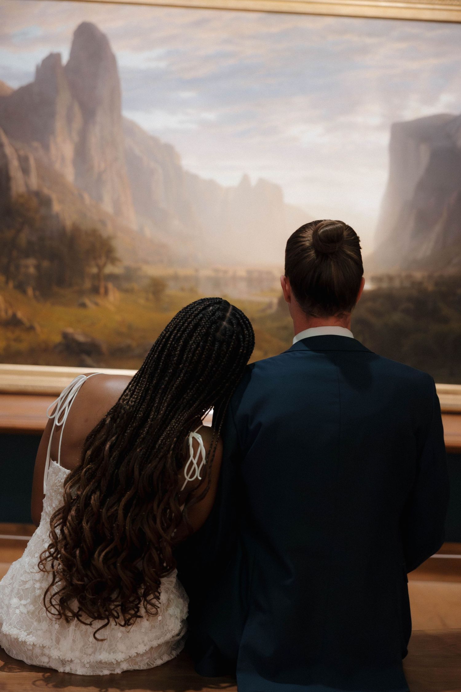 A couple admiring a landscape painting together in an art museum.