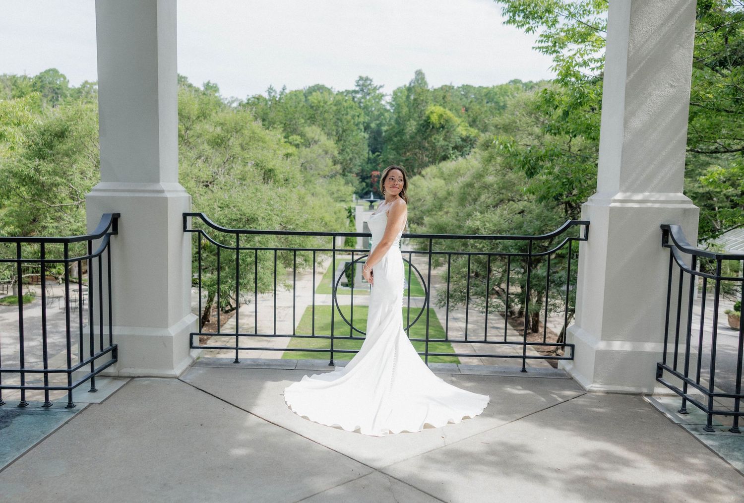 Architectural wedding venue with white columns and black railings against green landscape.