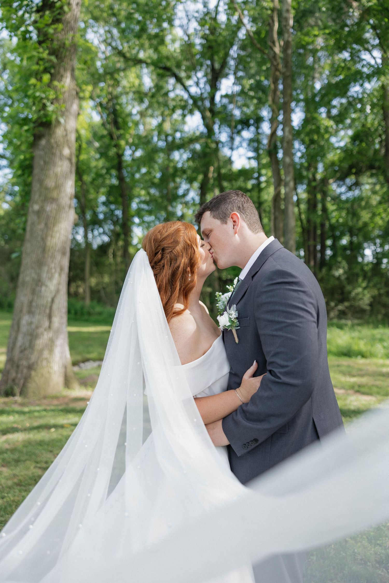 A romantic moment captured between newlyweds with flowing veil in a natural outdoor setting.