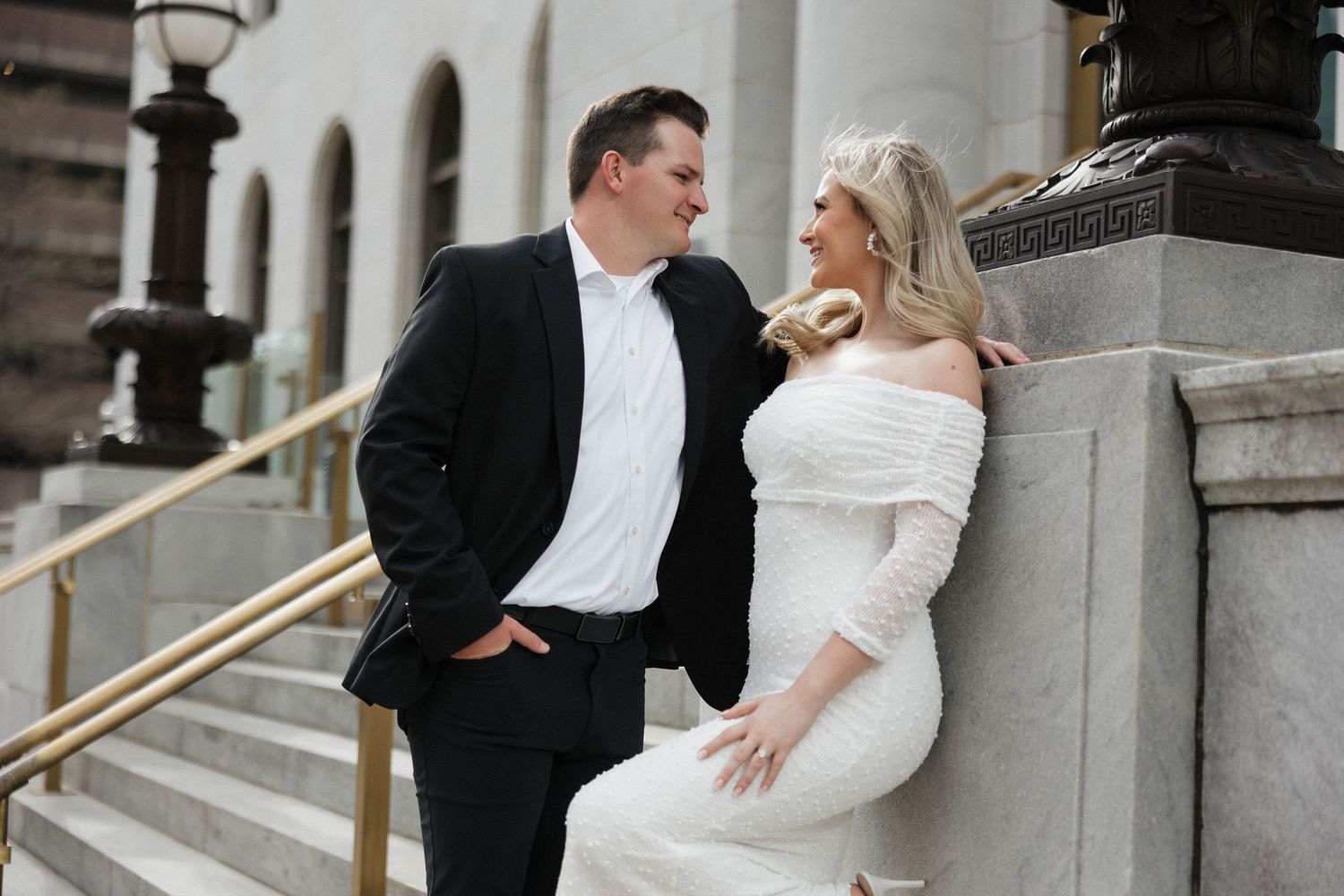 Elegant couple in wedding attire shares candid moments on stone steps.