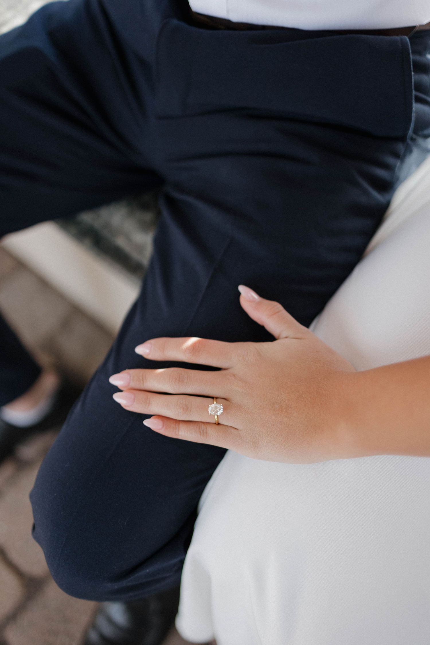 Close-up shot of an engagement ring on a hand against formal attire.