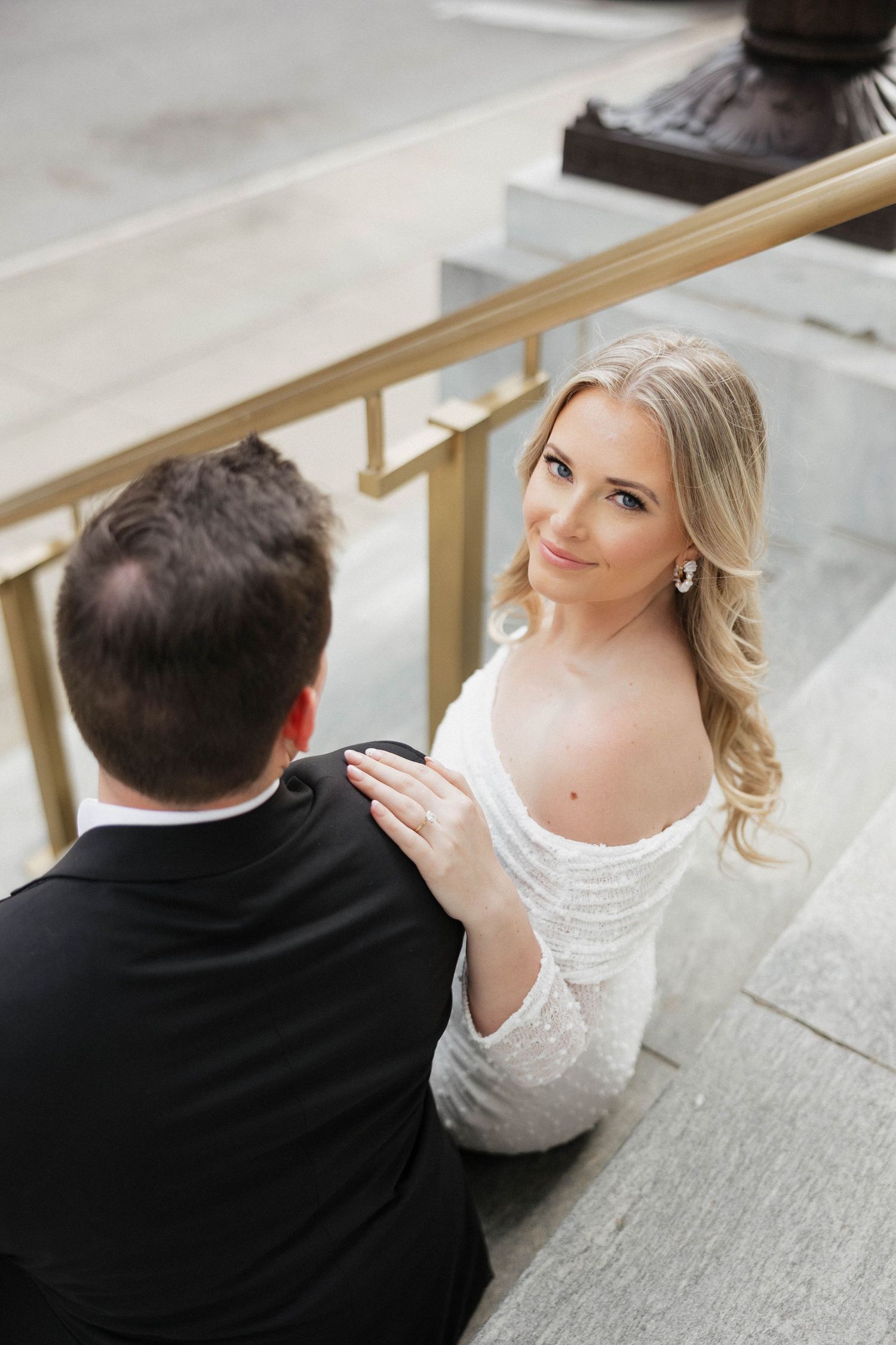 A couple in formal attire share a romantic first look moment on an outdoor staircase.