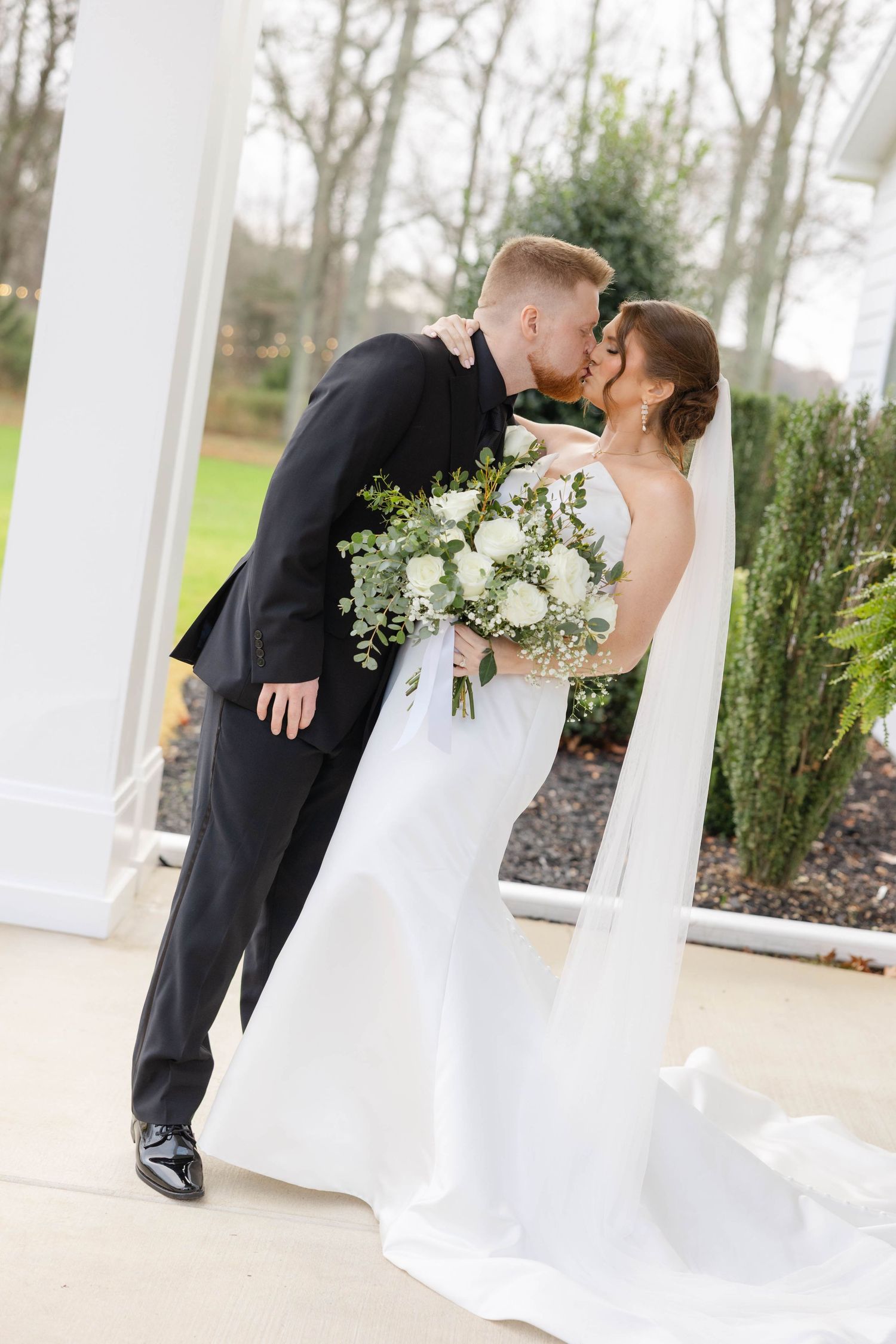 Romantic wedding couple sharing intimate moment on white columned porch.