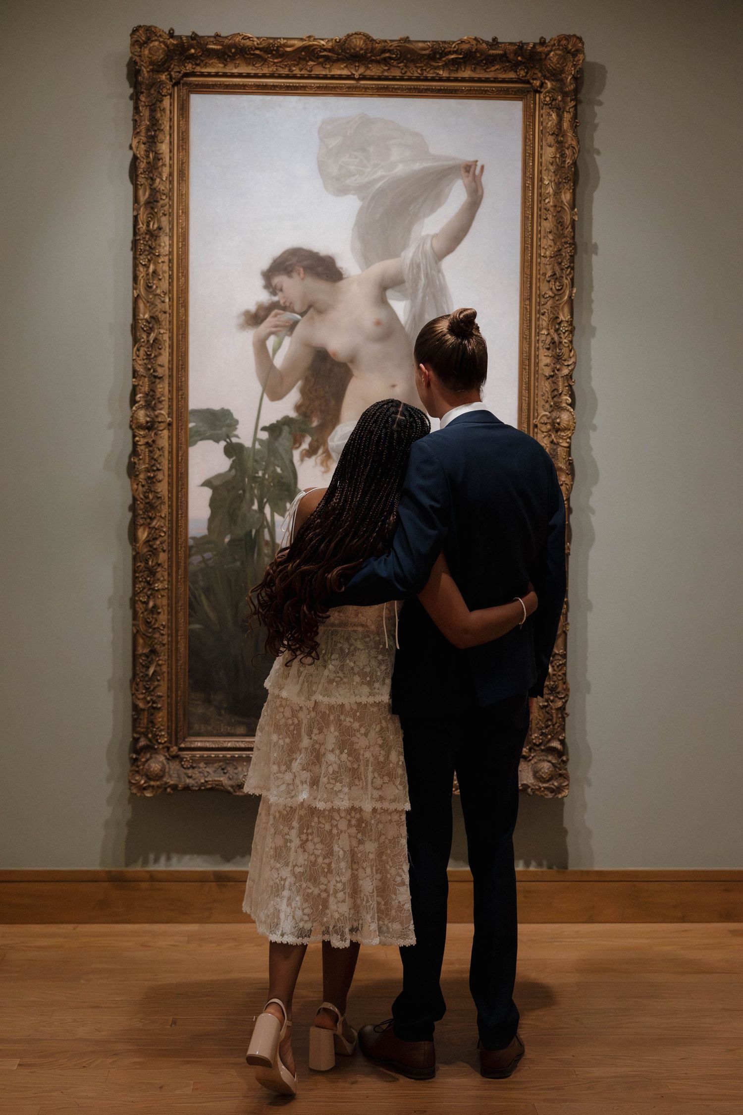 A couple viewing classical artwork in an ornate gold frame at an art gallery.
