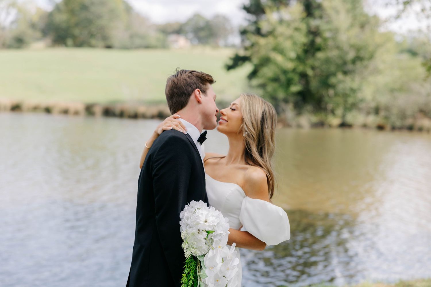A romantic wedding couple shares intimate kisses by a serene lakeside setting.