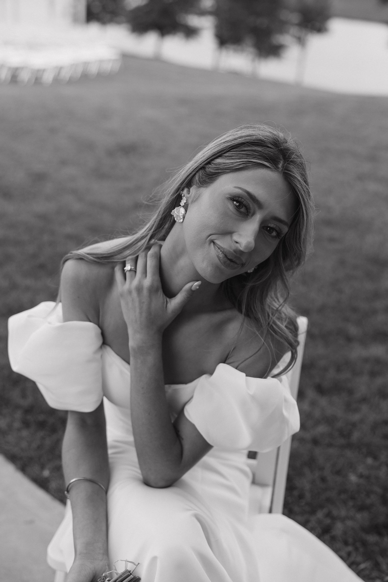 Woman in white dress poses gracefully on grassy hillside.