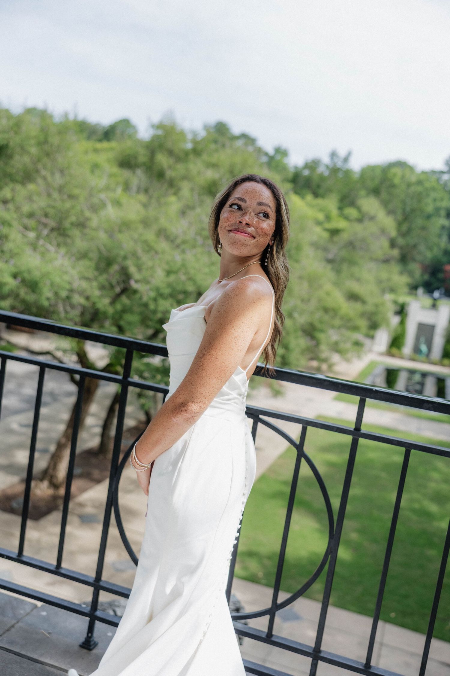Elegant bridal portrait against black railing with natural outdoor backdrop.
