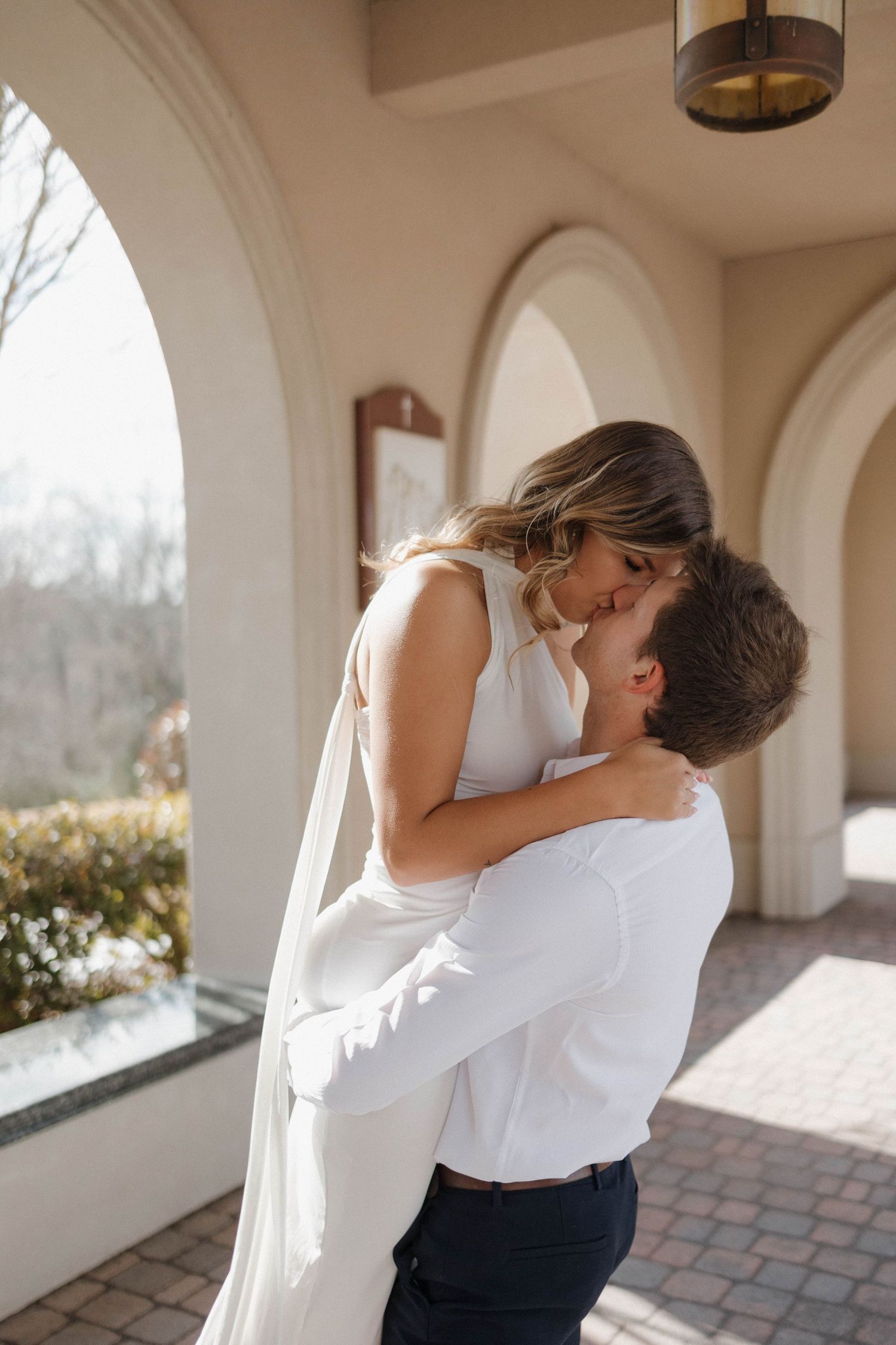 Romantic embrace captured in sunlit arched colonnade.