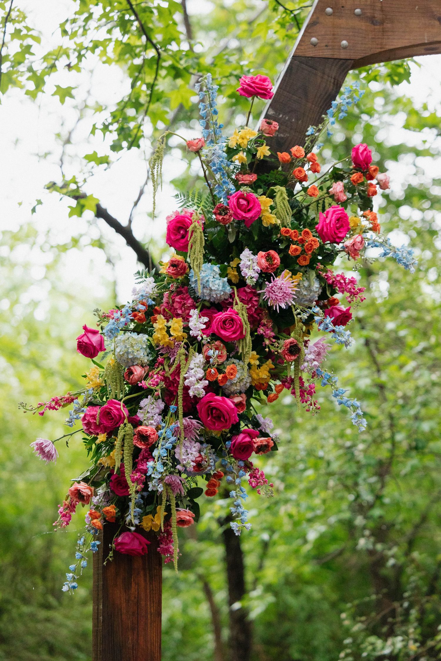 Vibrant floral arrangements with pink and orange blooms decorate a wooden outdoor structure.